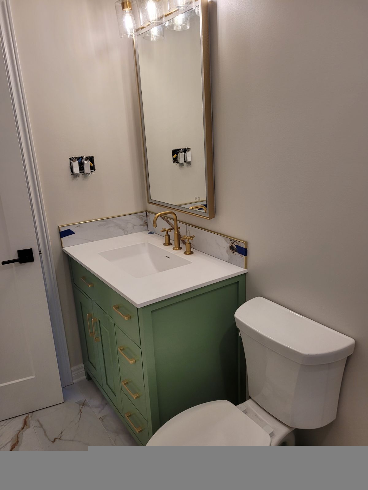 Small bathroom with mint green vanity, white sink, gold faucet, and wall mirror.