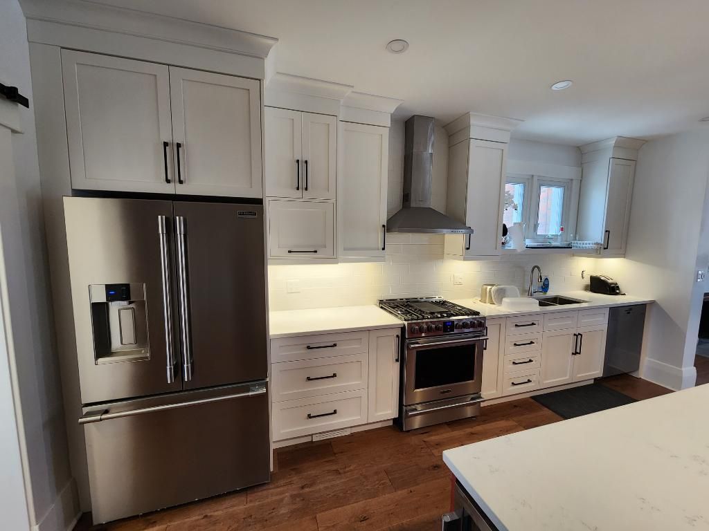 Modern kitchen with a large white island, red cabinets, hanging black lights, and a central dark support pole