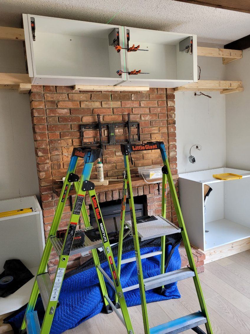 Ladders and tools in a room with exposed brick wall and partially installed white cabinets