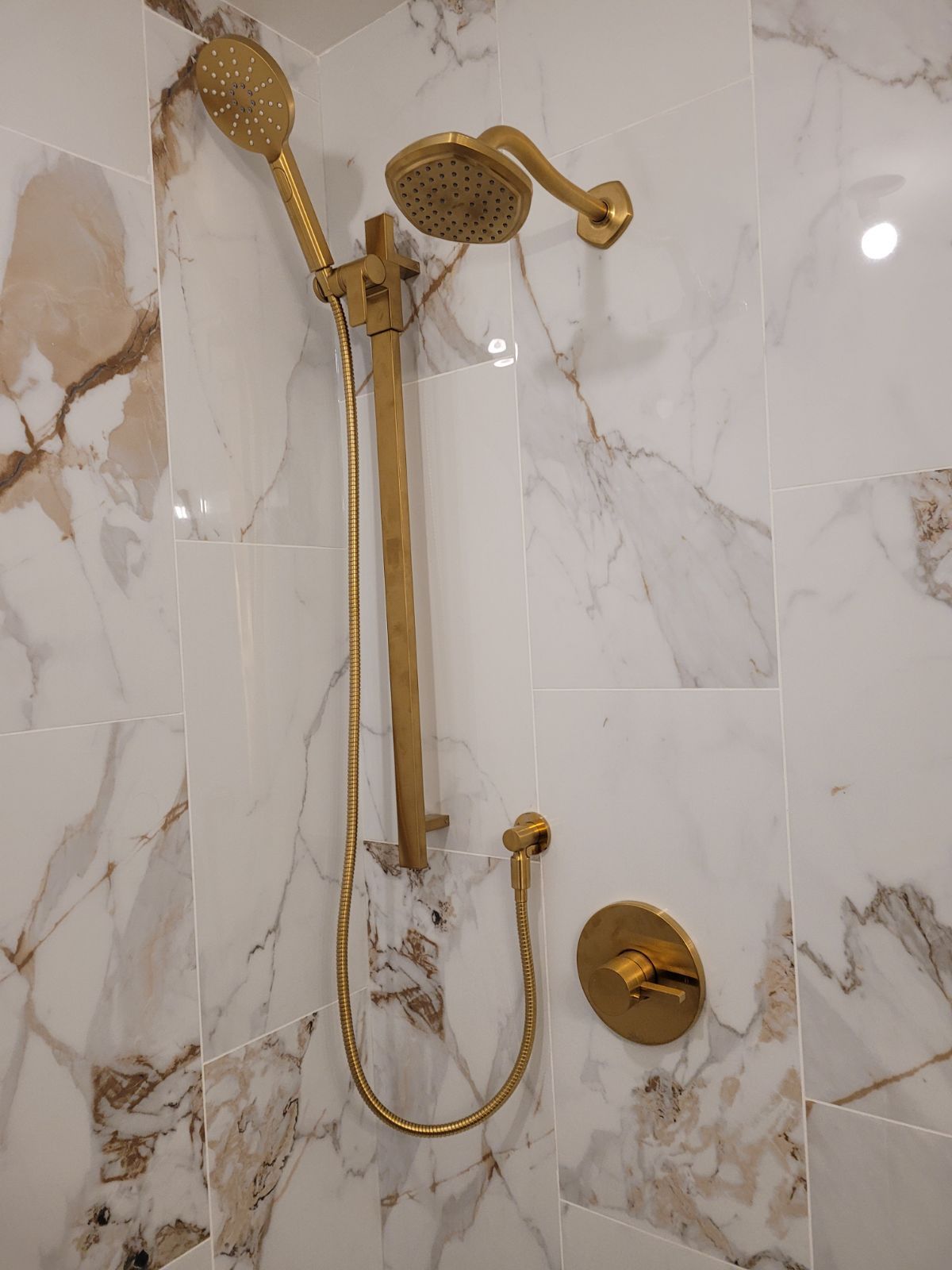 Gold shower fixture in a marble-tiled bathroom wall