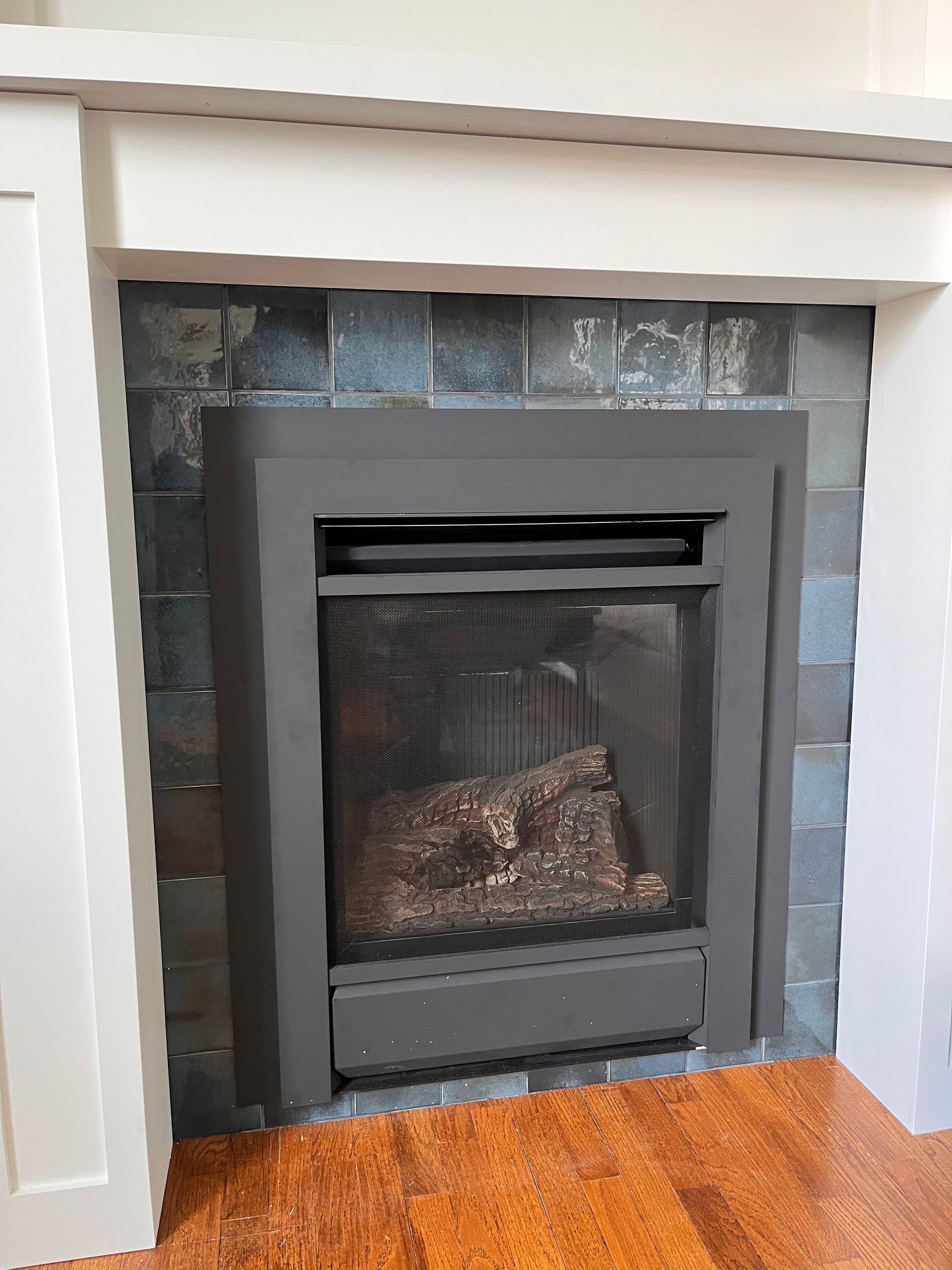 Modern electric fireplace inset in a white mantel with dark tiled surround and hardwood floor