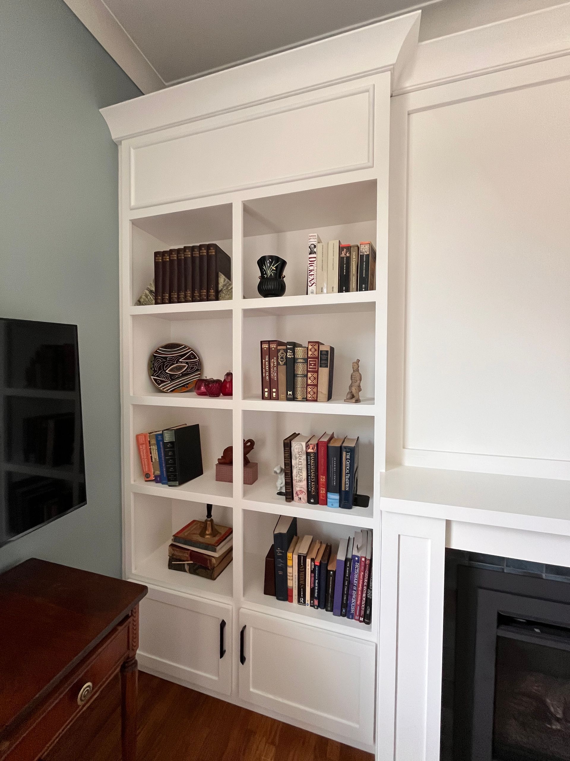 Built-in white bookshelf with books and decor beside a fireplace in a bright living room