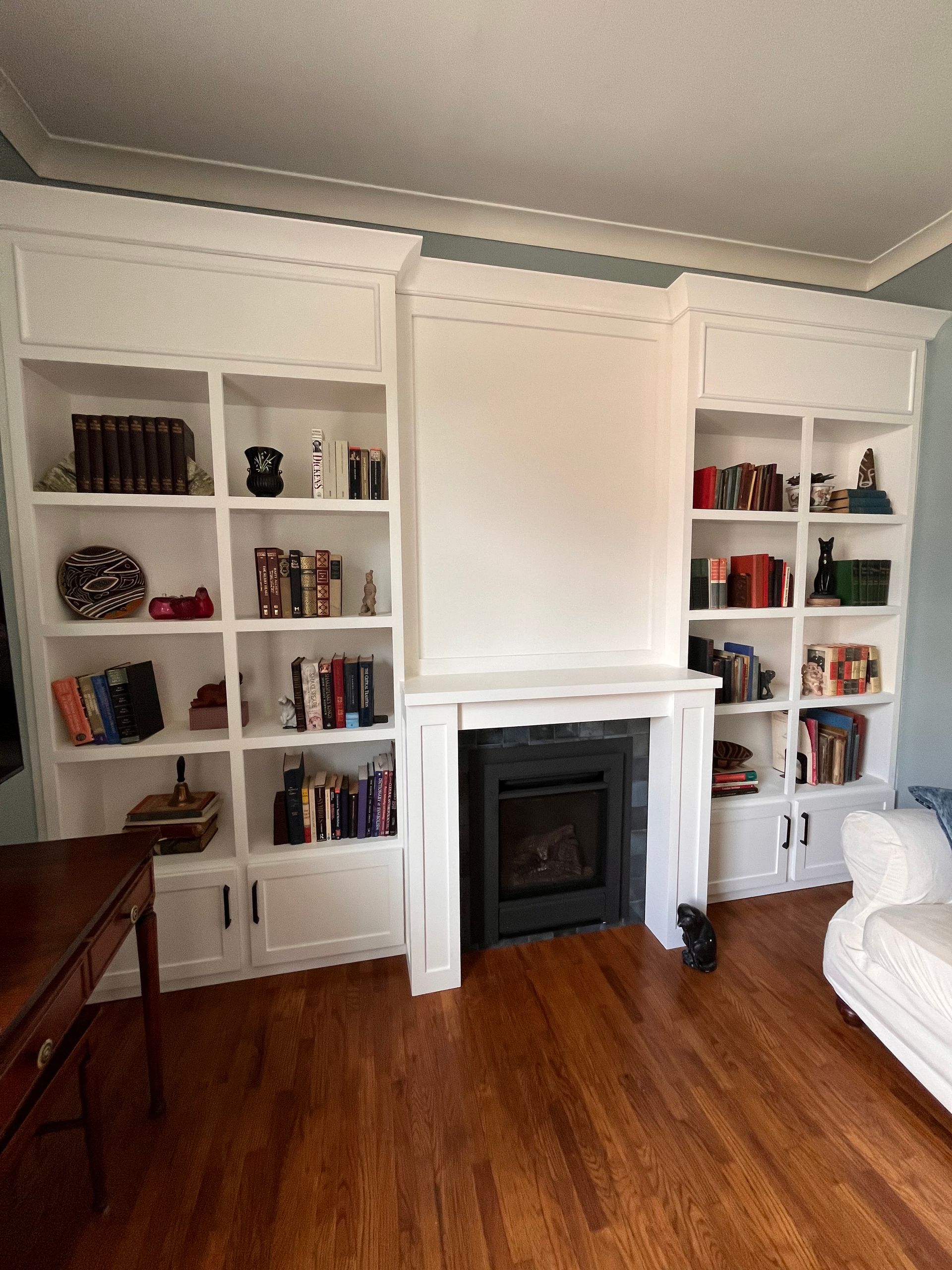 Living room with white built-in bookshelves flanking a fireplace, hardwood floor, and a white sofa at right.
