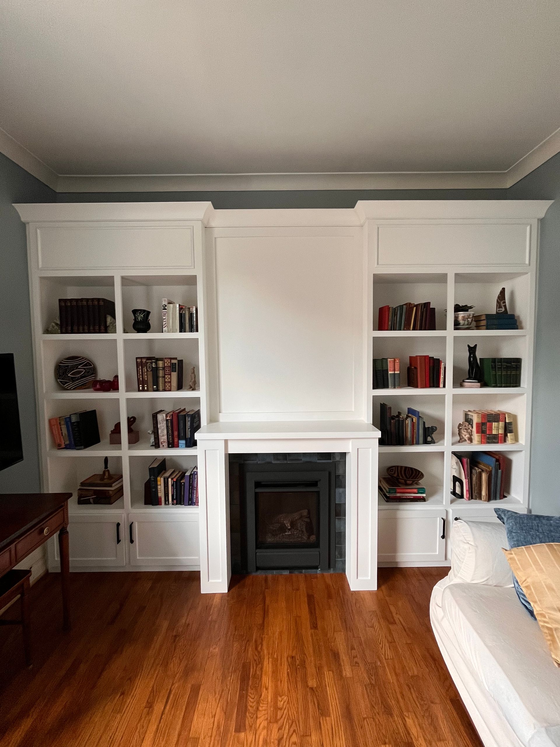 White built-in bookshelves and fireplace in a living room with hardwood floors.
