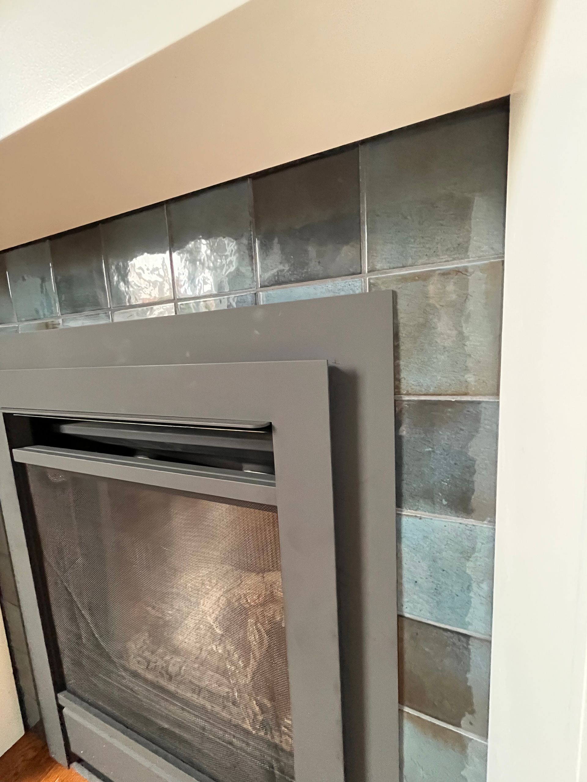 Modern fireplace with gray tile surround and reflective glass front in a beige wall alcove