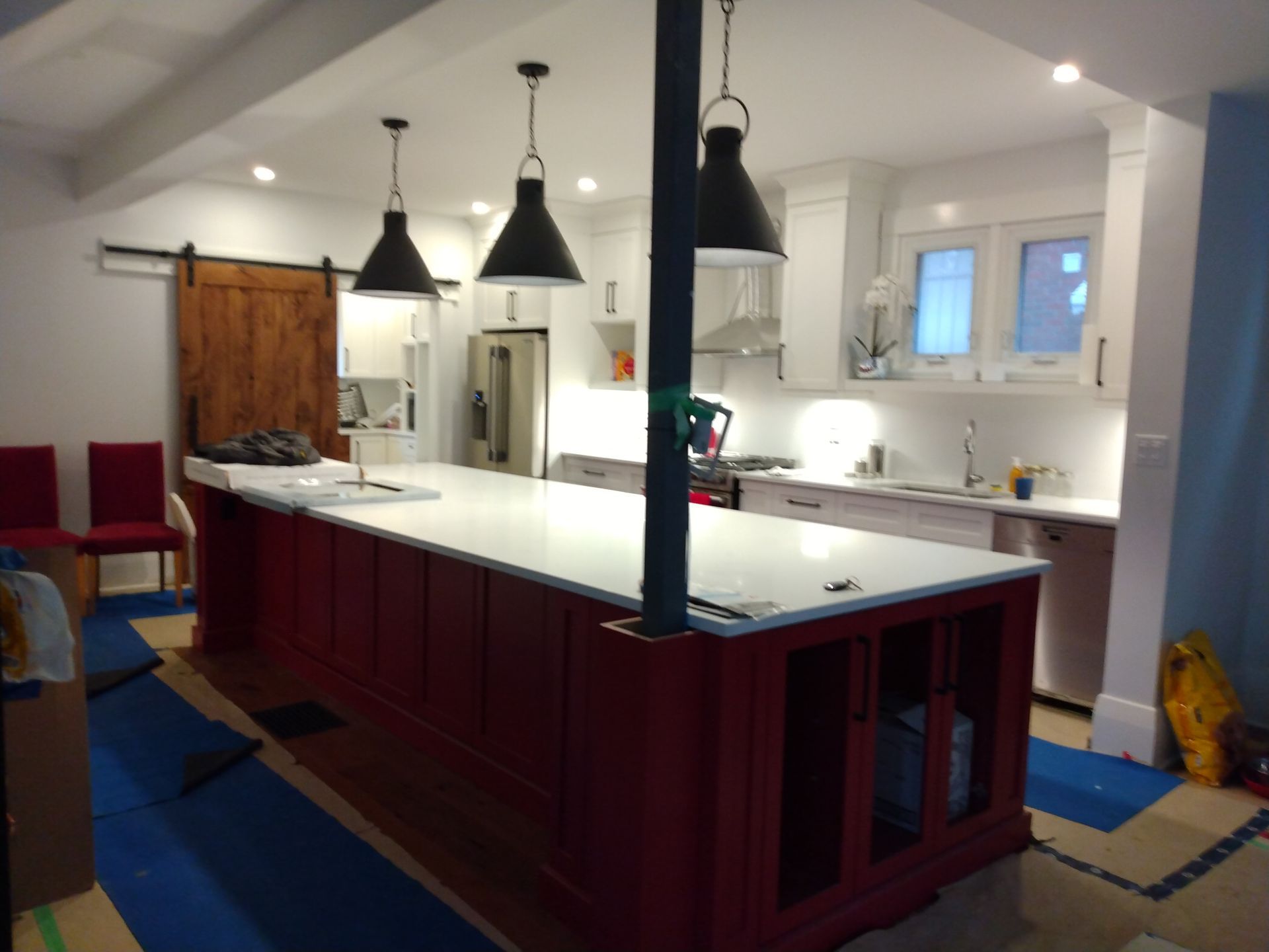 Modern kitchen with a large red island, white countertops, and black pendant lights under a sloped ceiling
