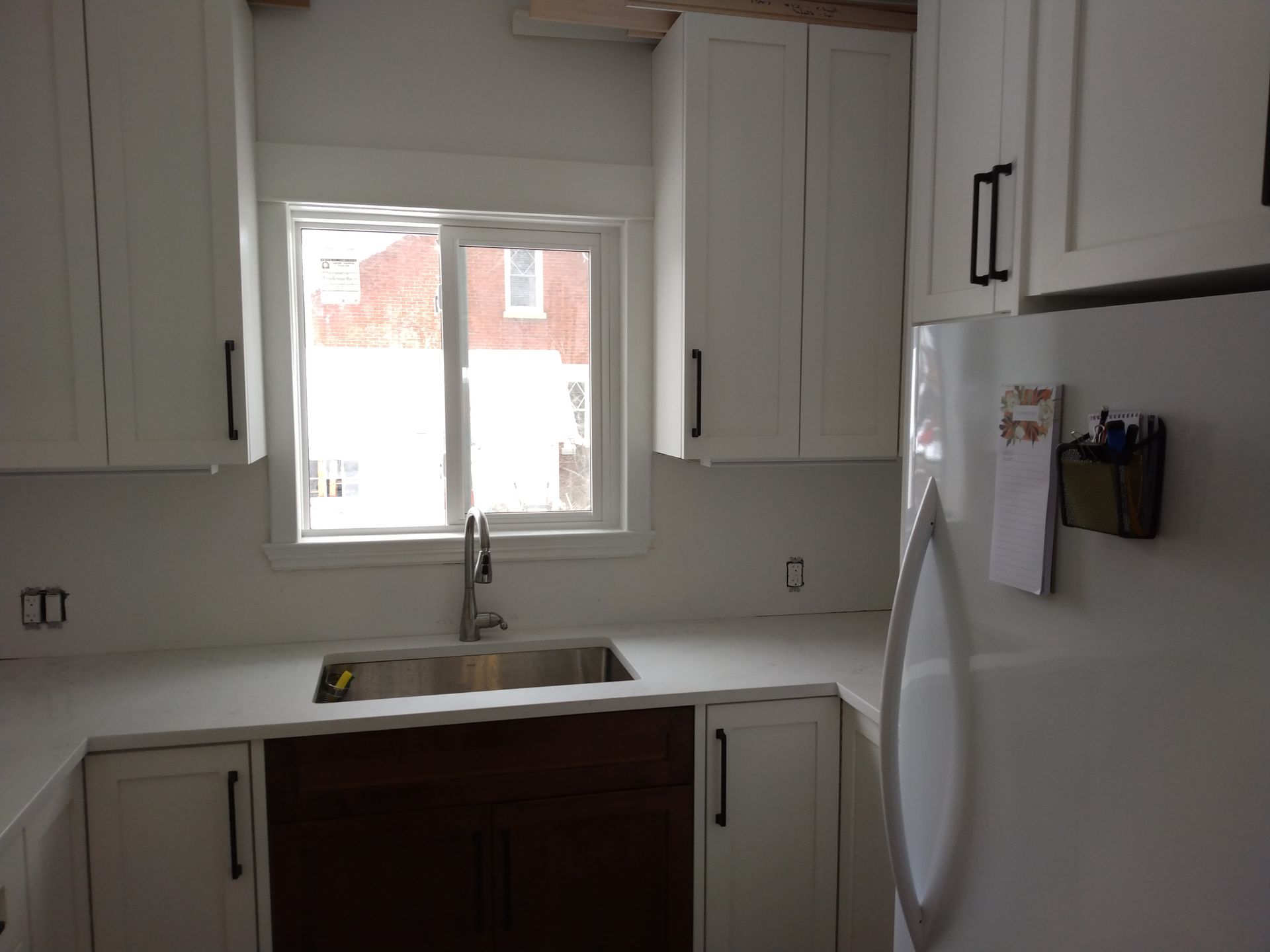 Bright kitchen with white cabinets, sink under a window, and a white refrigerator on the right.