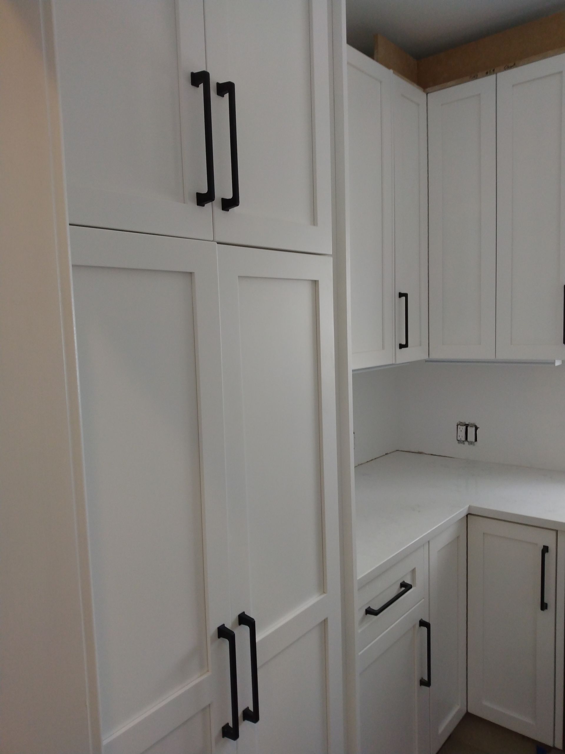 White kitchen with tall cabinets, black handles, and light countertops in a corner layout