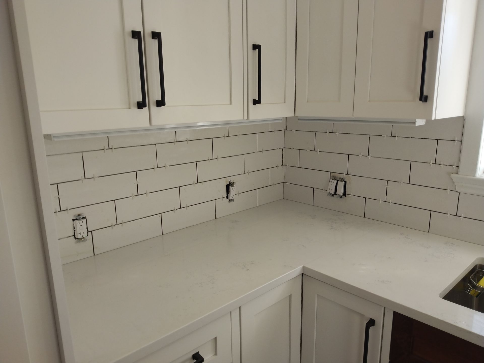 White kitchen corner with cabinets, white subway tile backsplash, and light countertop