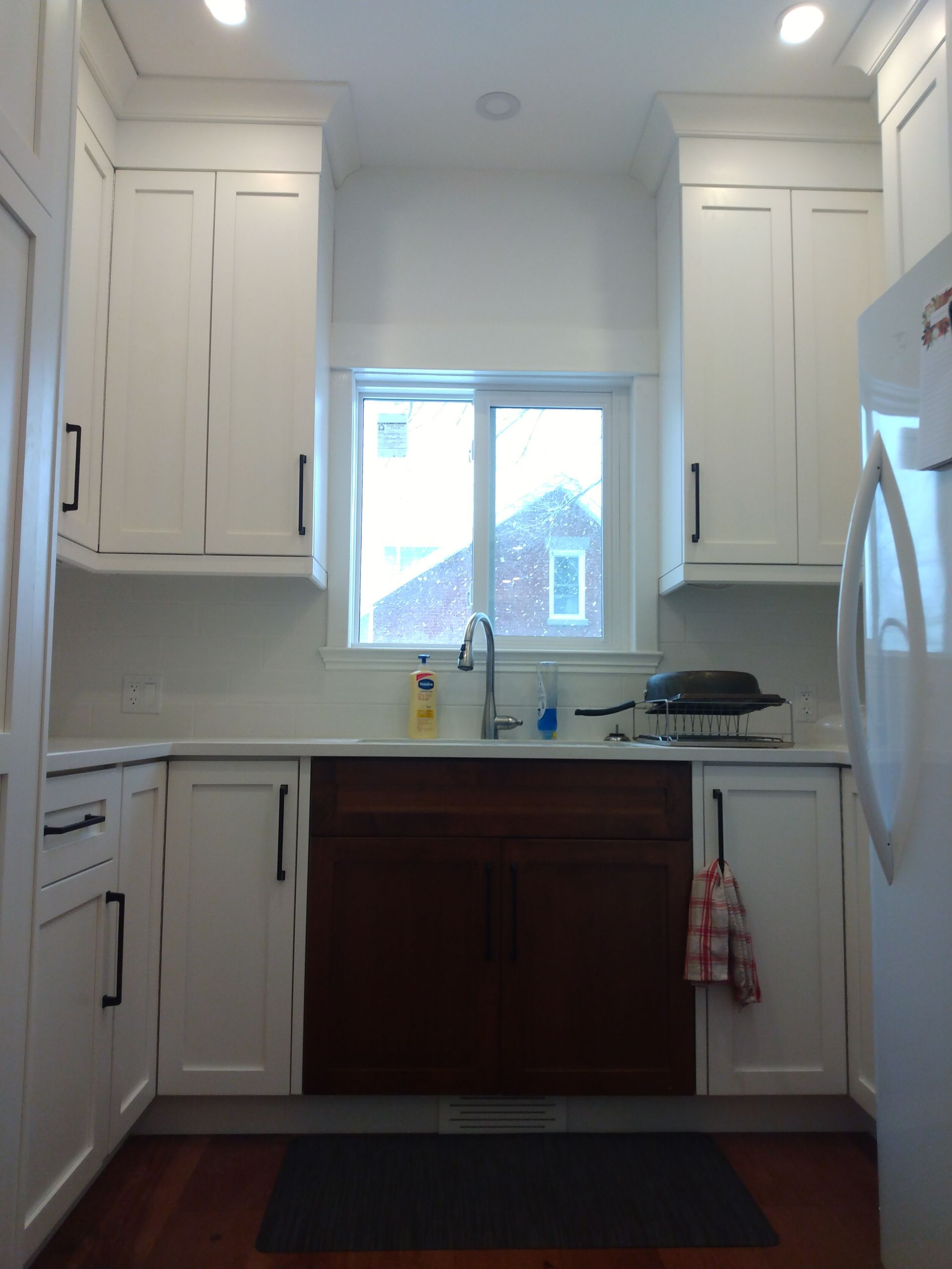 Bright kitchen with white cabinets, dark countertop, central window, sink, and refrigerator on the right.