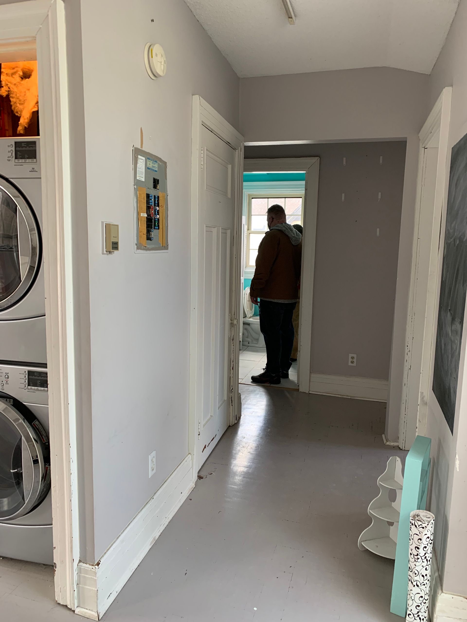Hallway with laundry closet on the left and a person standing at the far end near an open door.