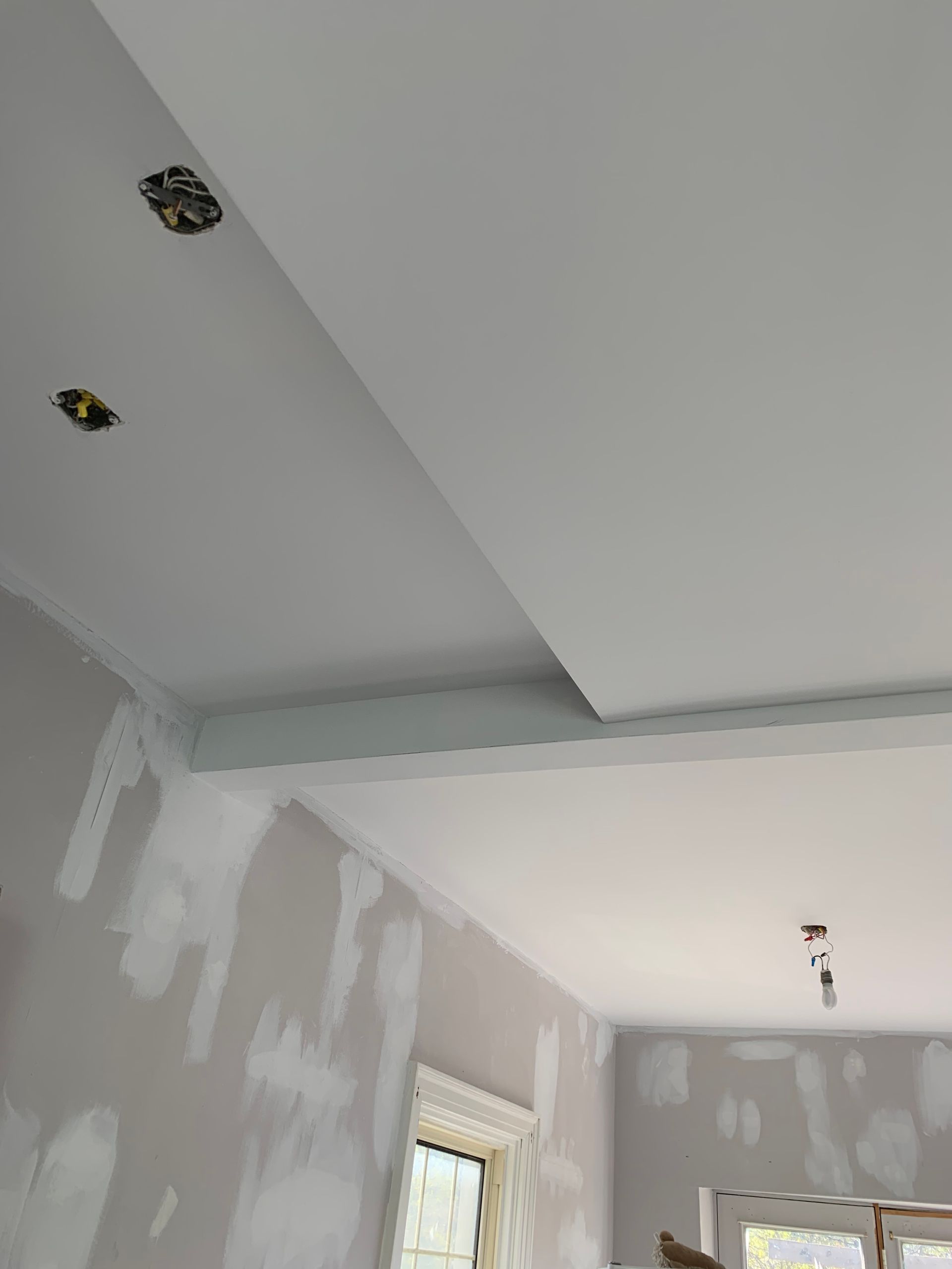 Interior room with white walls and ceiling patches, a window, and exposed light fixture holes during renovation