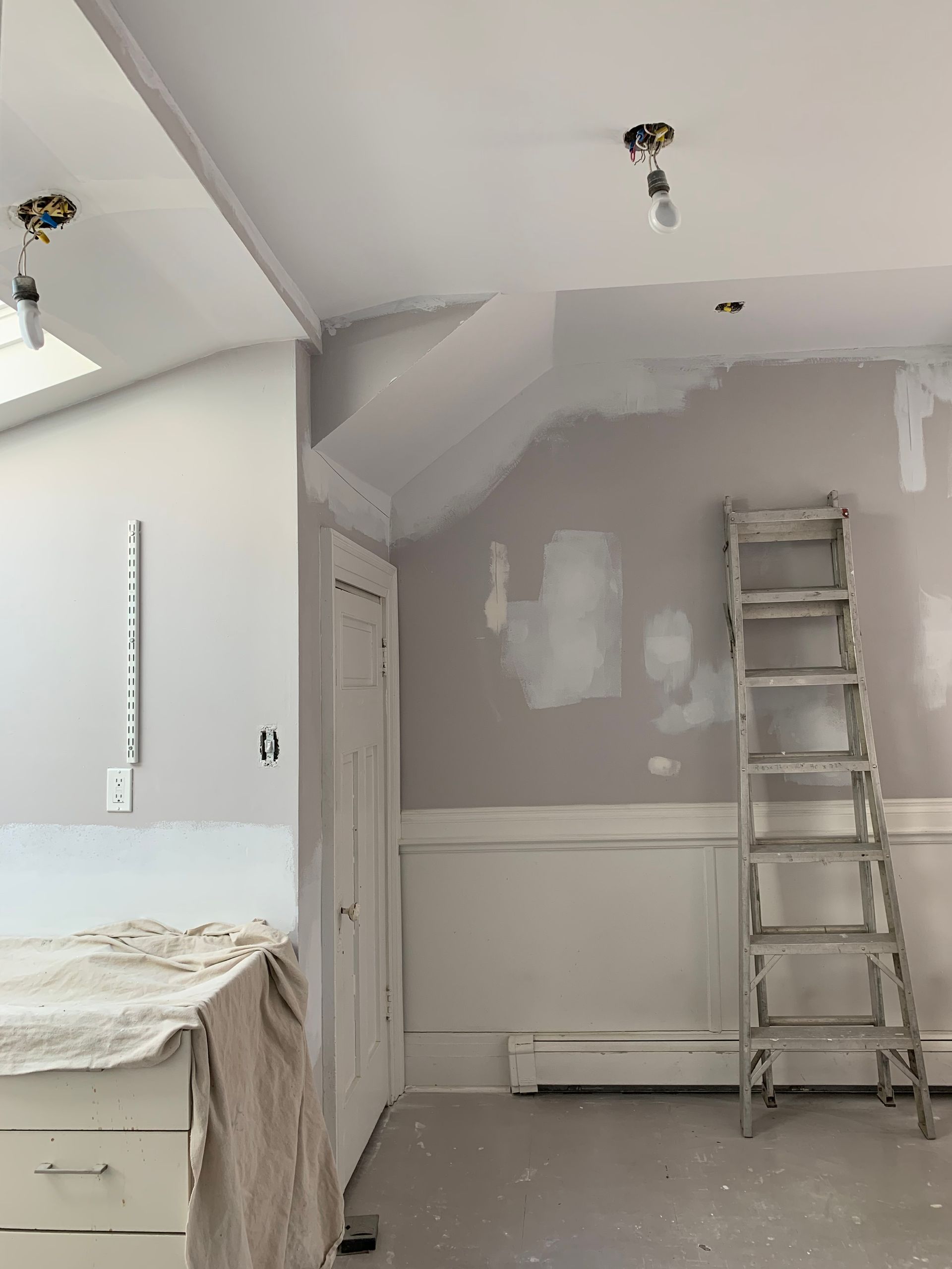 Partially painted bedroom with ladder, sloped ceiling, and bed under renovation