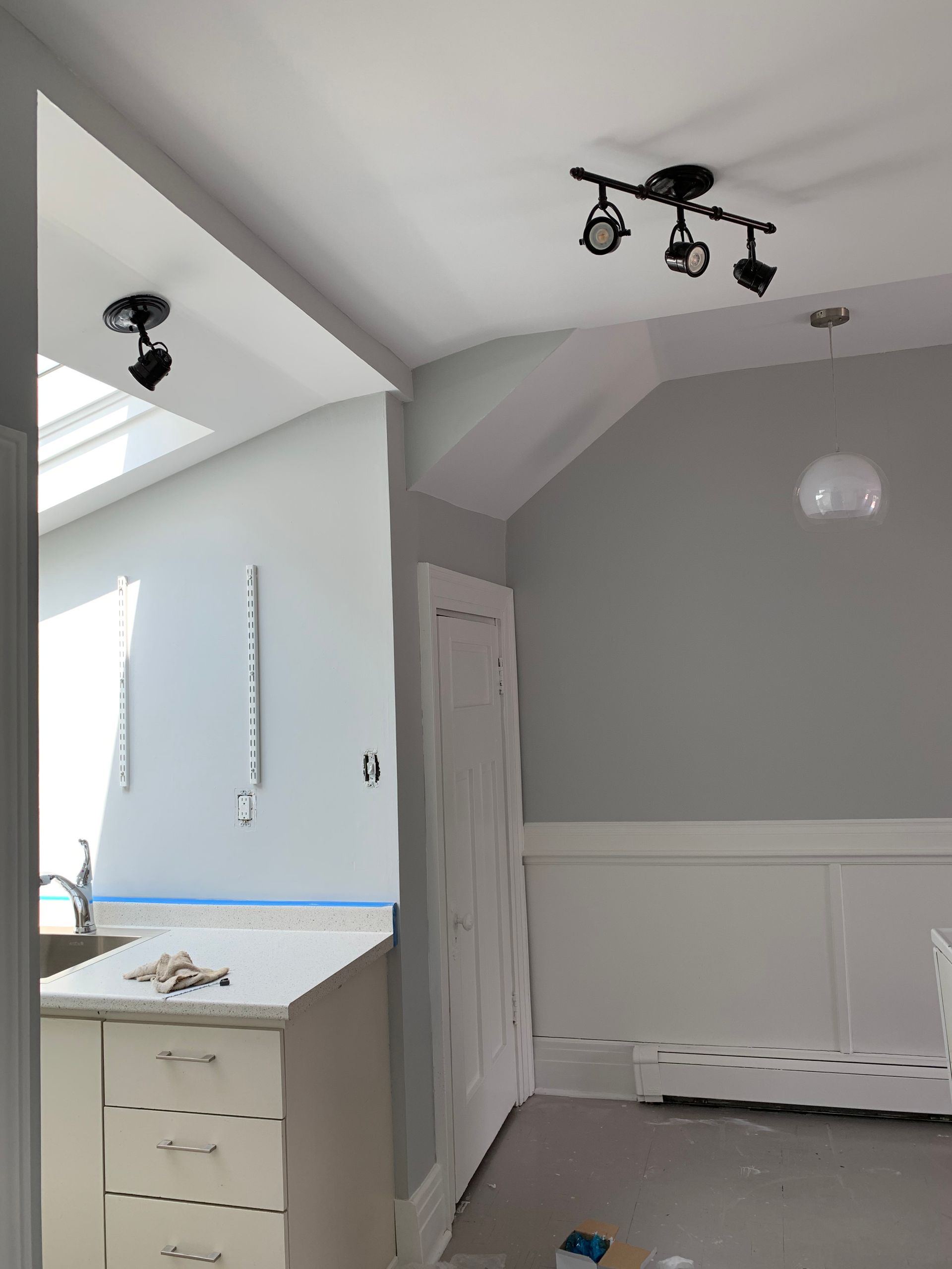 Empty gray room with white trim, a small cabinet, and ceiling lights near a kitchen pass-through.