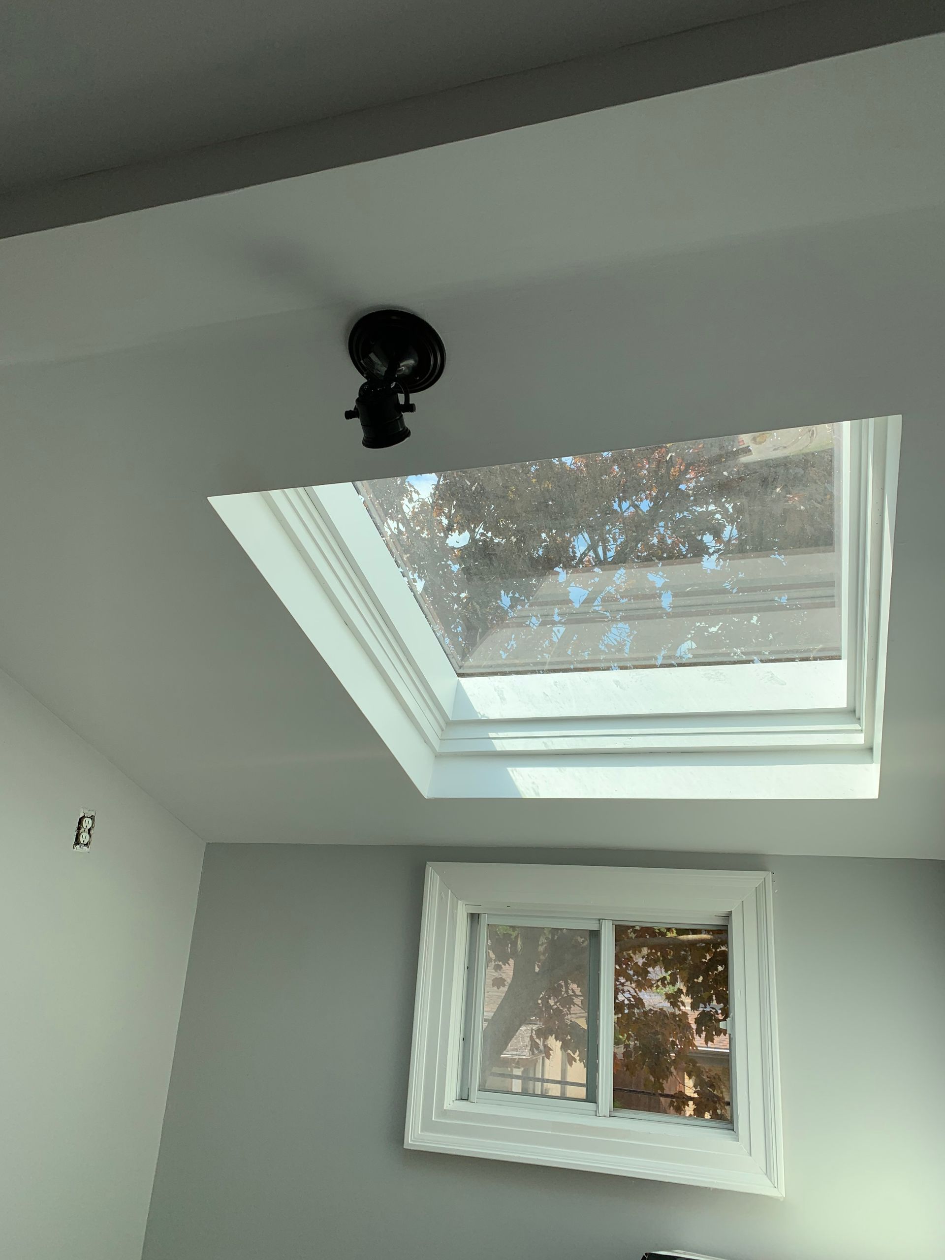 Skylight and small window on a white wall, with a black ceiling fixture above the skylight.