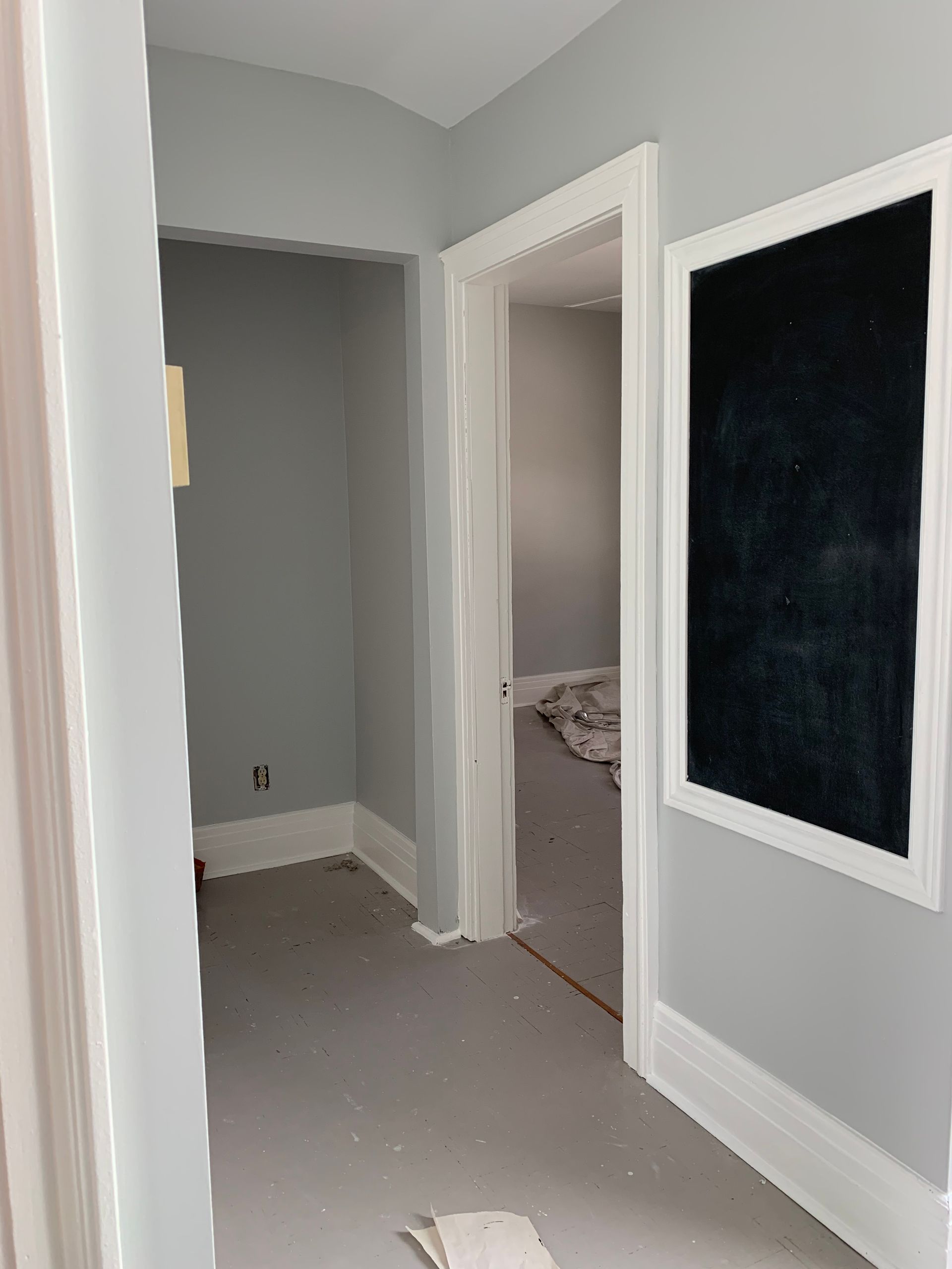 Empty gray hallway with open doorways and a large black wall panel on the right