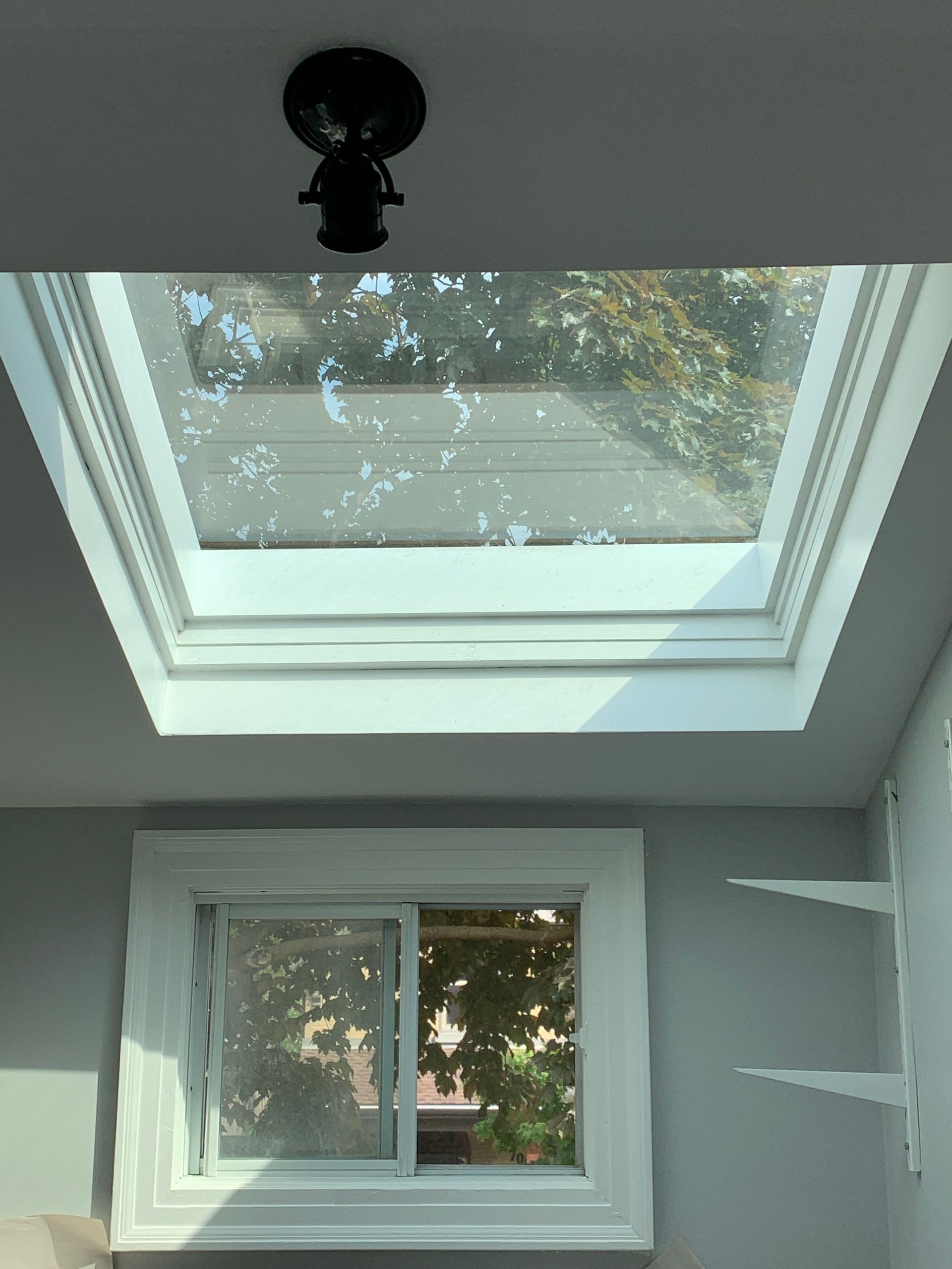 Skylight and small window in a gray room, with a ceiling light and built-in shelf on the right.
