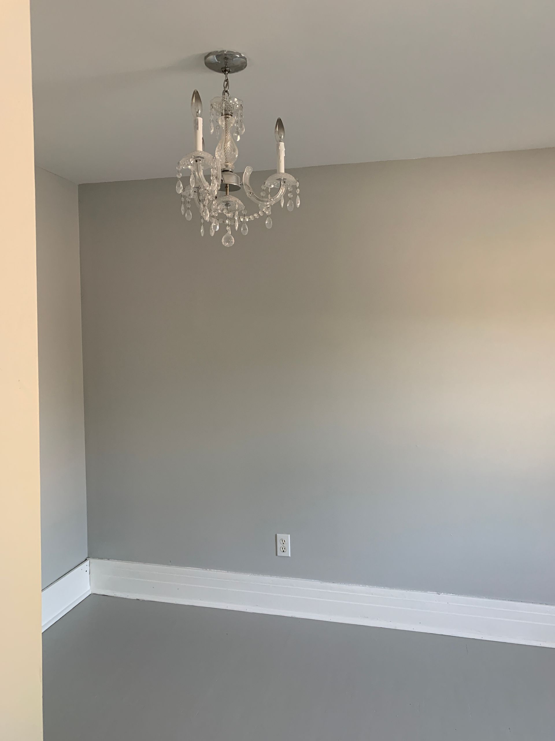 Empty gray room with white trim and a small chandelier hanging from the ceiling.