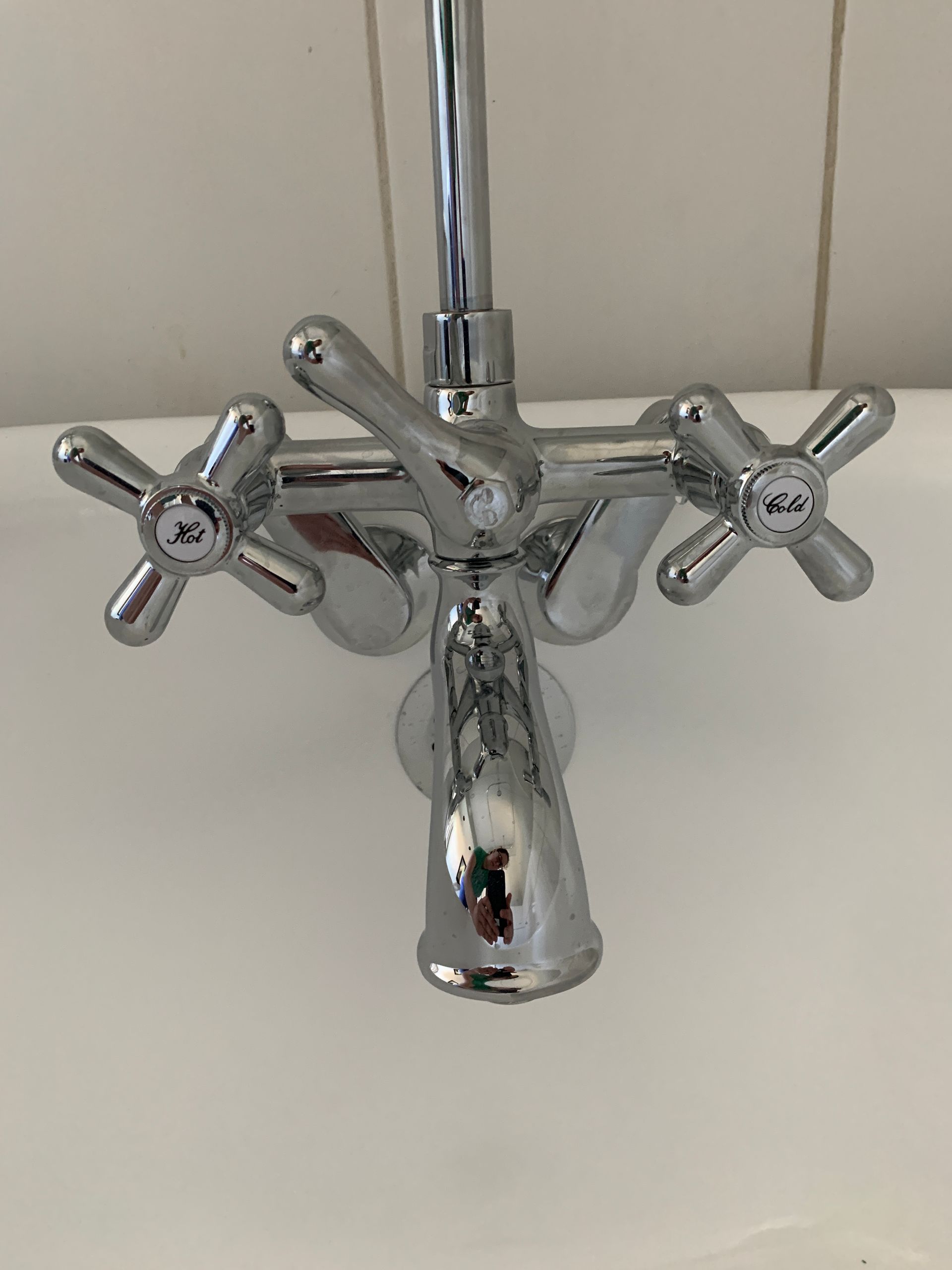 Chrome bathroom faucet with two cross handles and a central spout against a tiled wall