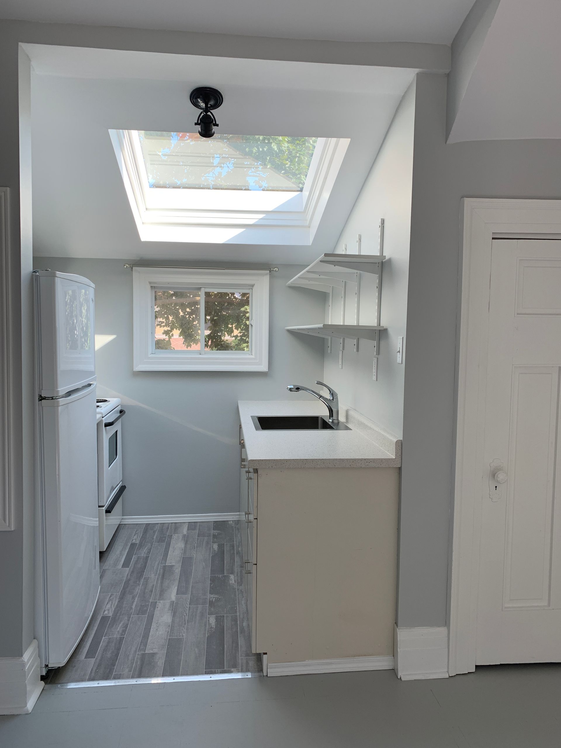 Small modern kitchen with skylight, white cabinets, gray floor, and a window above the sink.