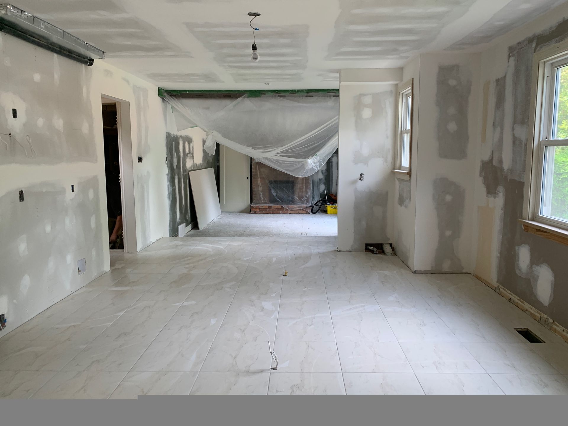 Renovated room with unfinished drywall, taped seams, white floors, and daylight from windows