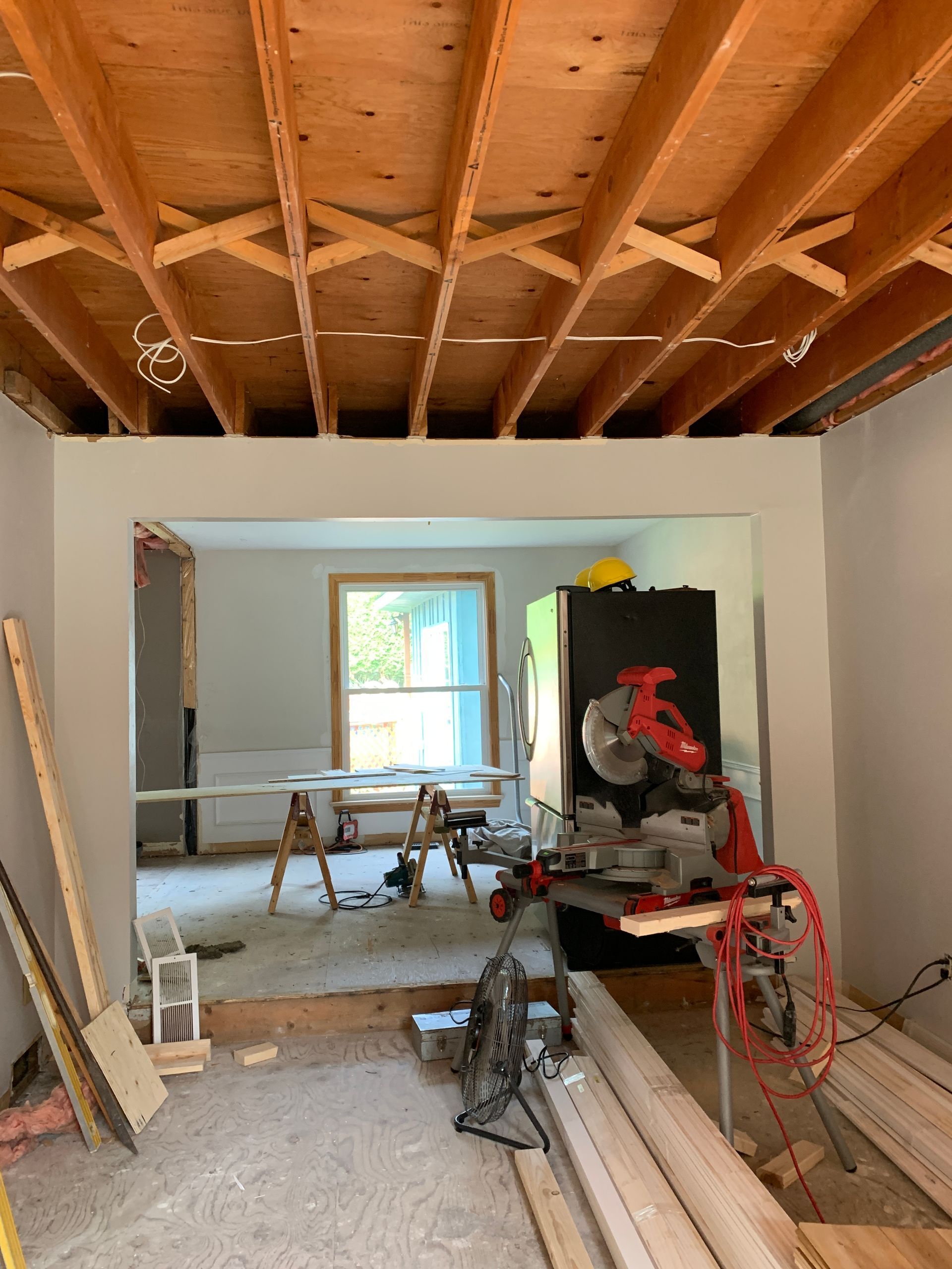 Renovation site with exposed ceiling joists, tools, lumber, and a large saw in a room under construction