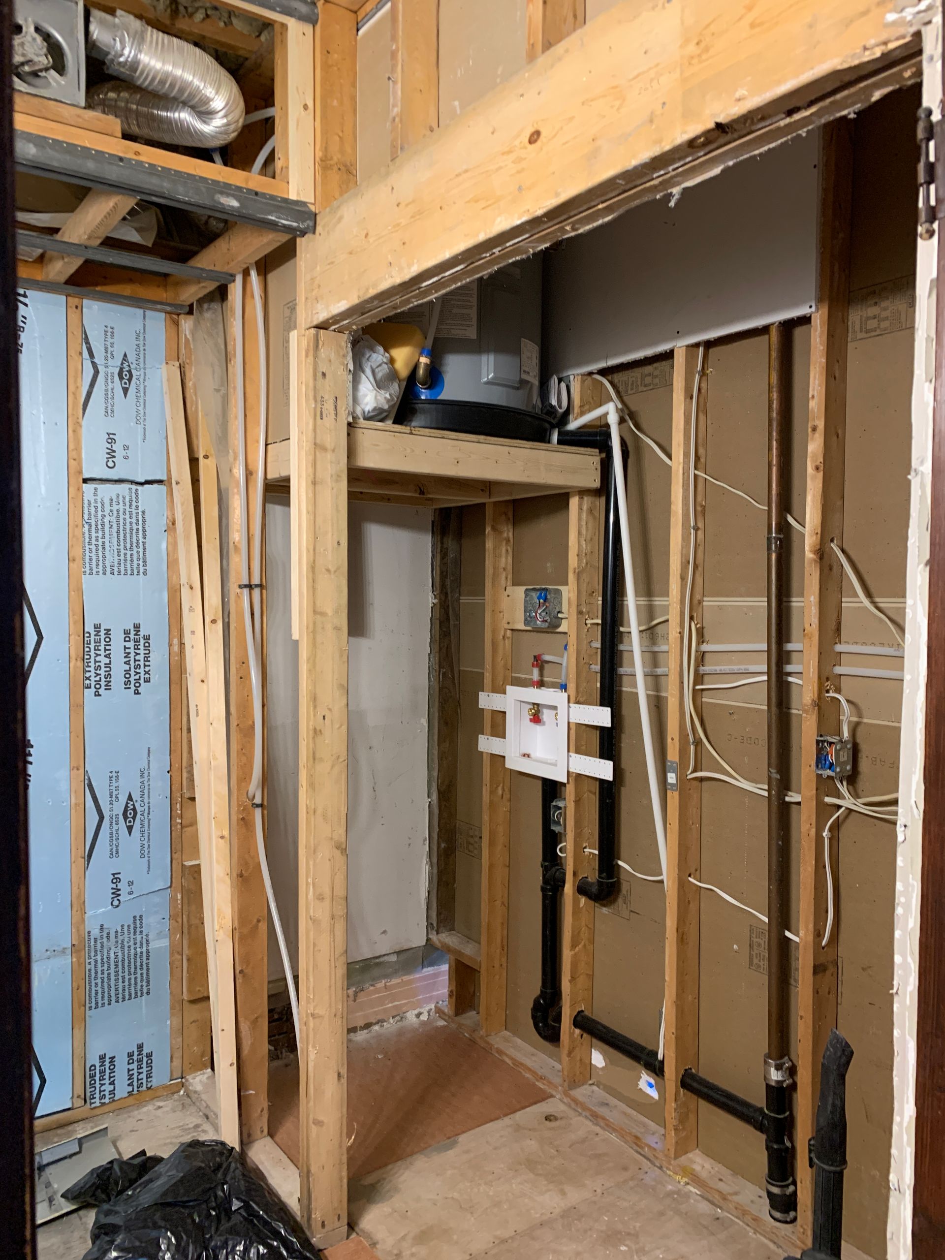 Partially finished bathroom wall framing with exposed pipes, wiring, and a vent duct above