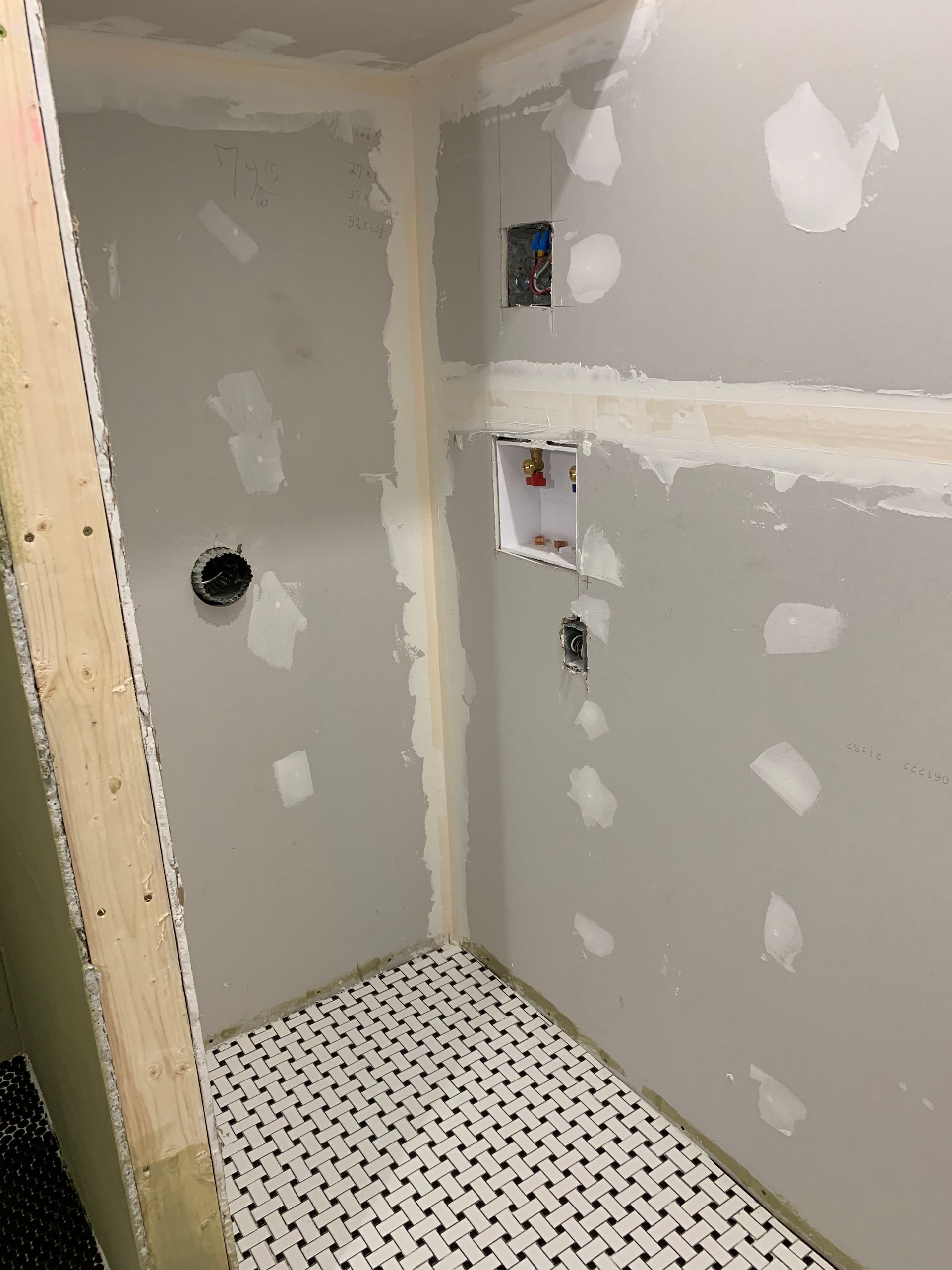 Unfinished bathroom shower stall with gray drywall, white patching, and a tiled floor.