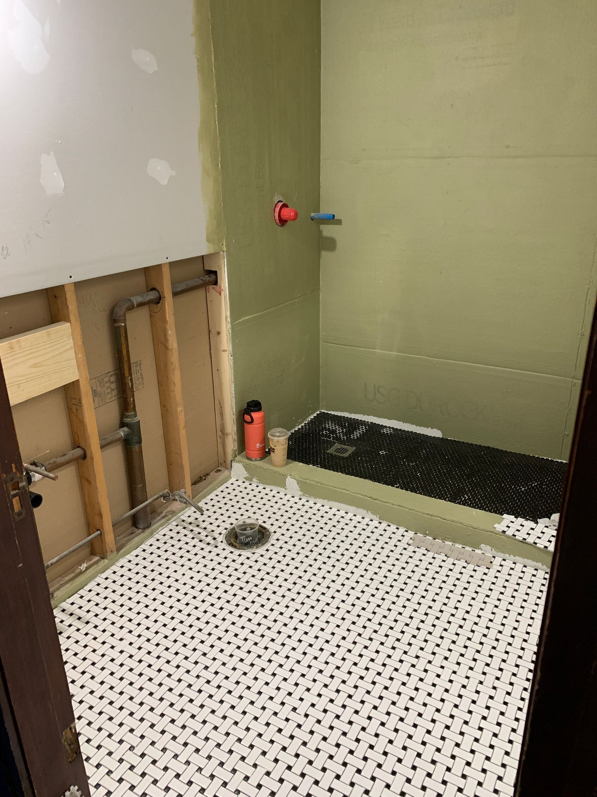 Bathroom shower under renovation with white mosaic floor, exposed wall studs, and tiled back wall