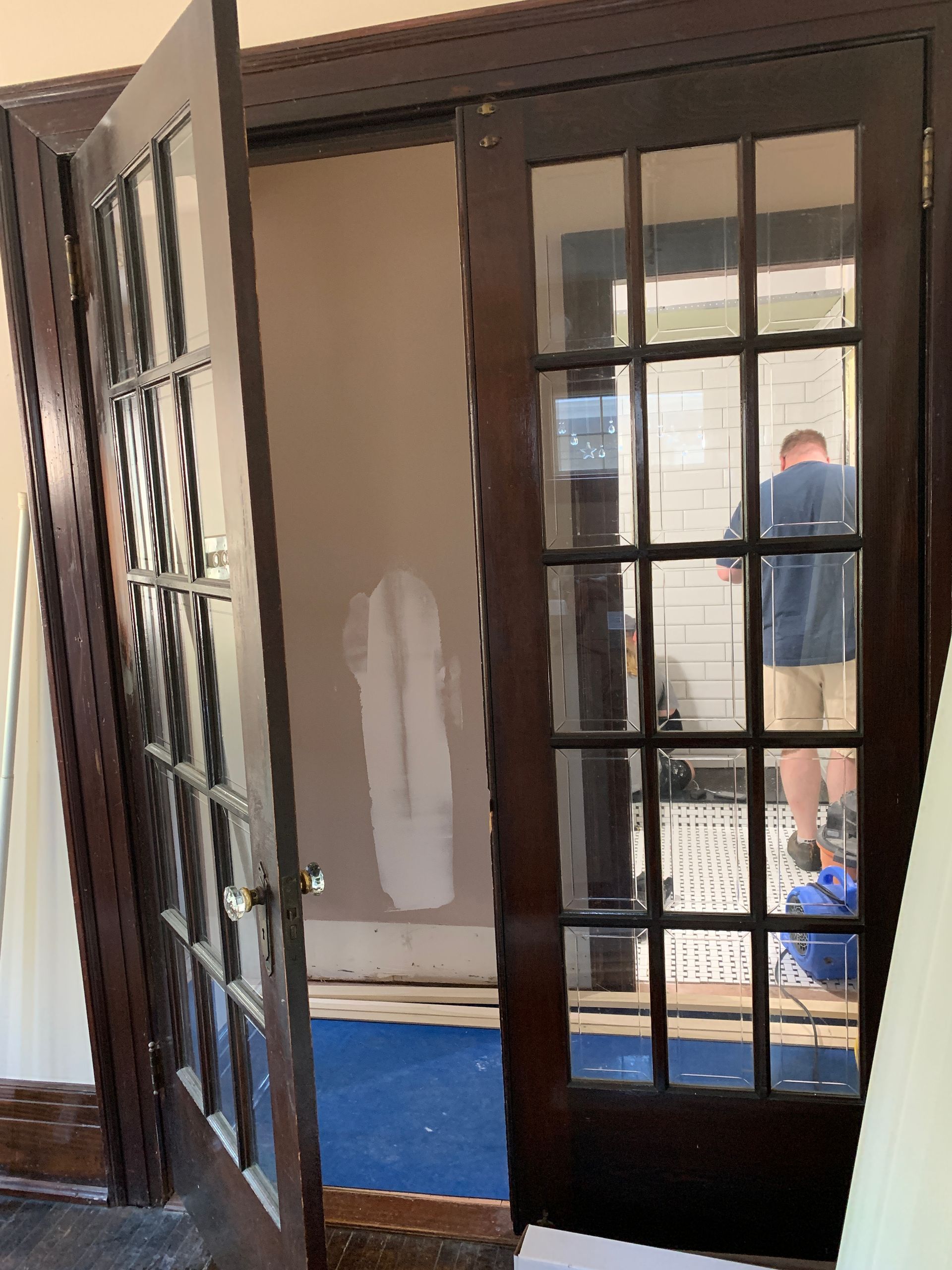 Open French doors into a room with blue carpet and a person visible in the background.