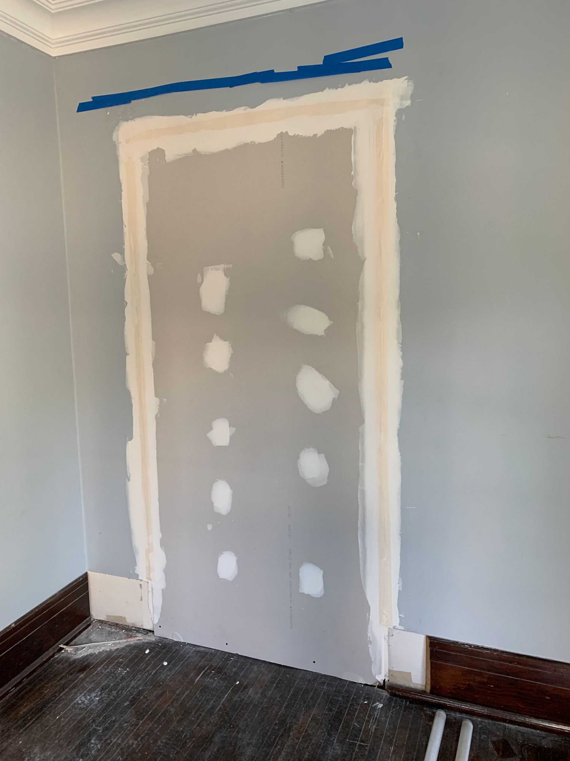Unfinished doorway framed with white caulk and drywall patches on a gray wall, taped at the top.