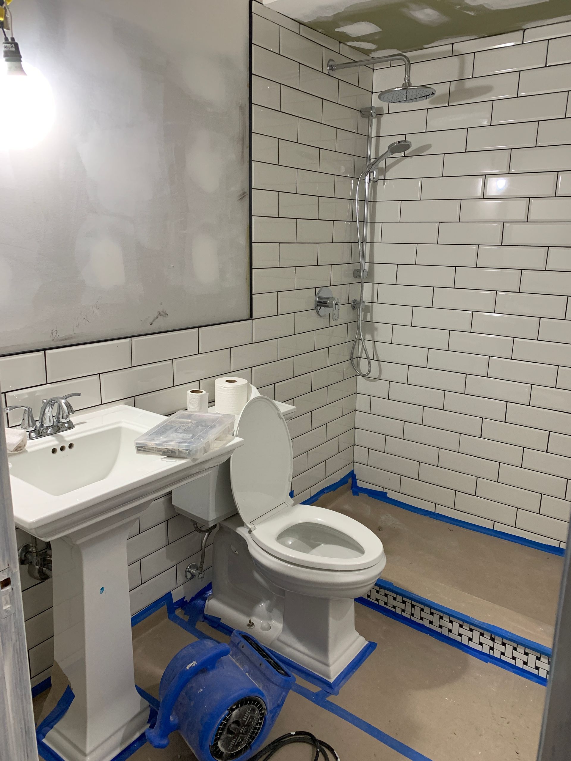 Small bathroom with a toilet, sink, and blue plumbing repairs, tiled walls, and a large mirror.