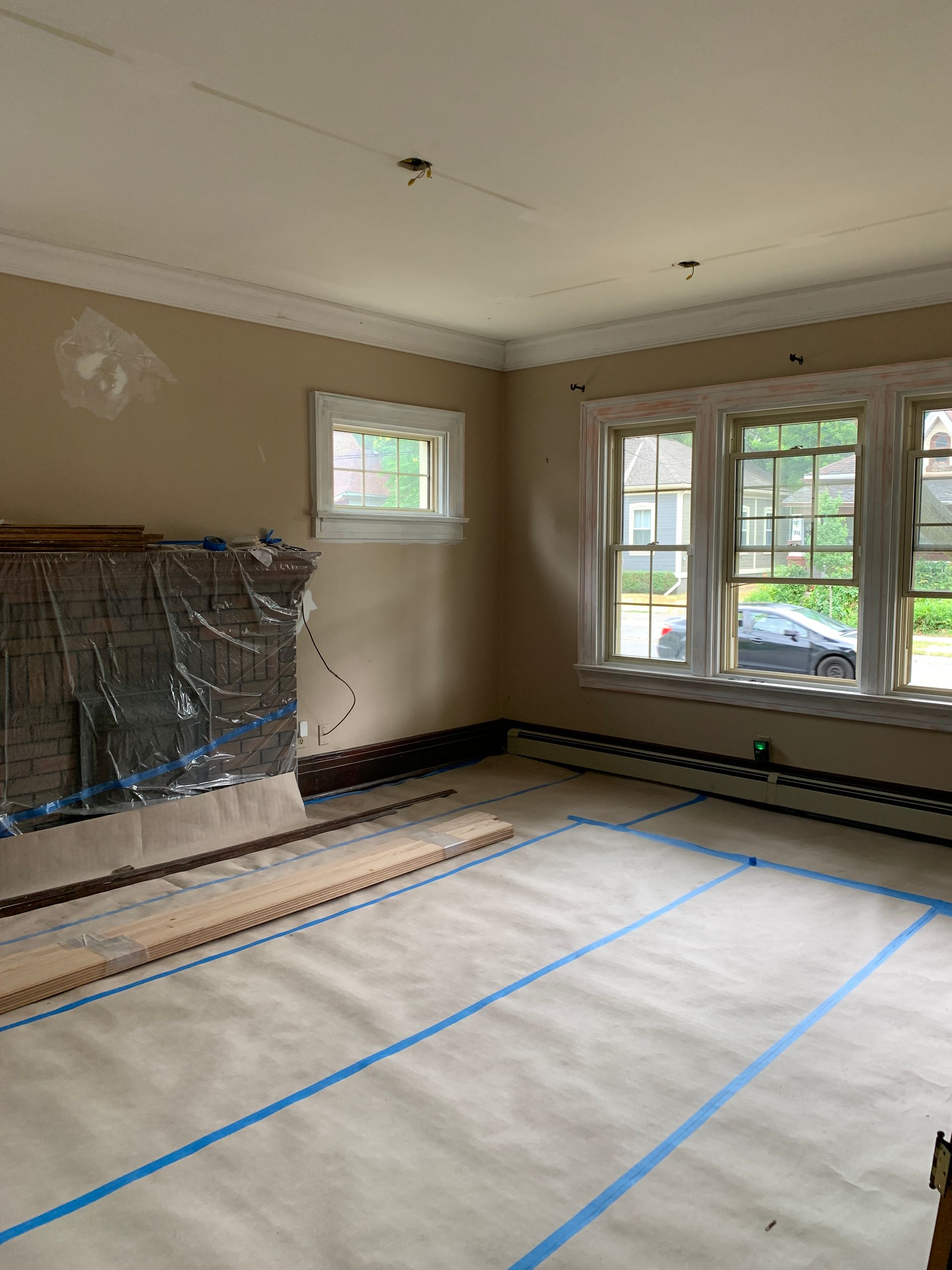 Empty room under renovation with floor covered in protective paper and blue tape, windows and doors at right.