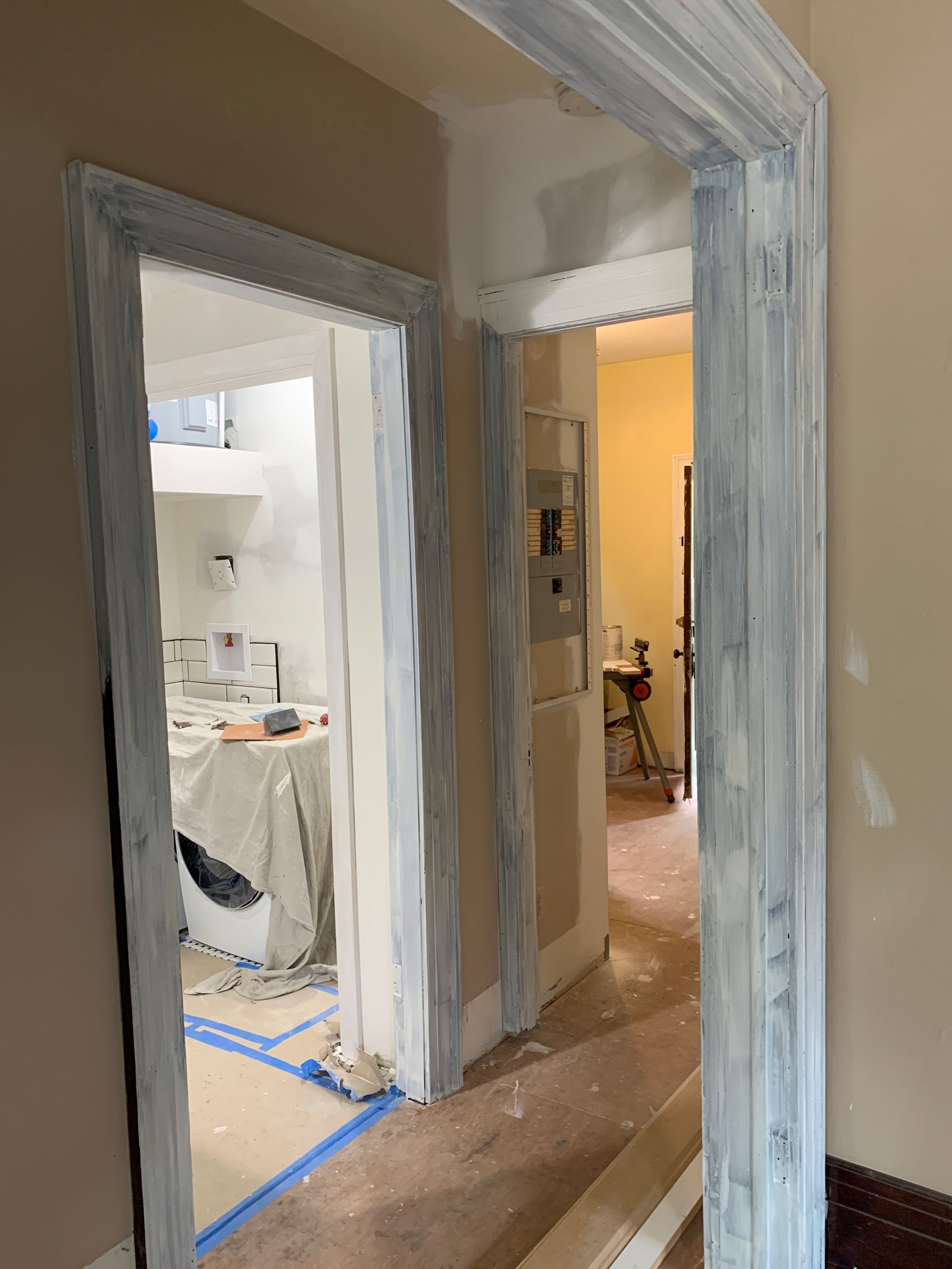 Narrow hallway under renovation with gray primer on door frames and blue painter’s tape on the floor.