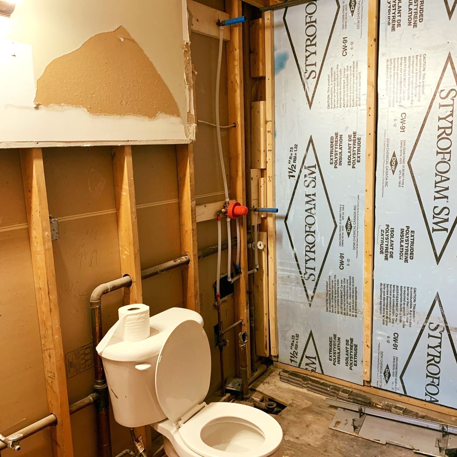 Partially renovated bathroom with exposed studs, toilet, and unfinished walls around a shower area