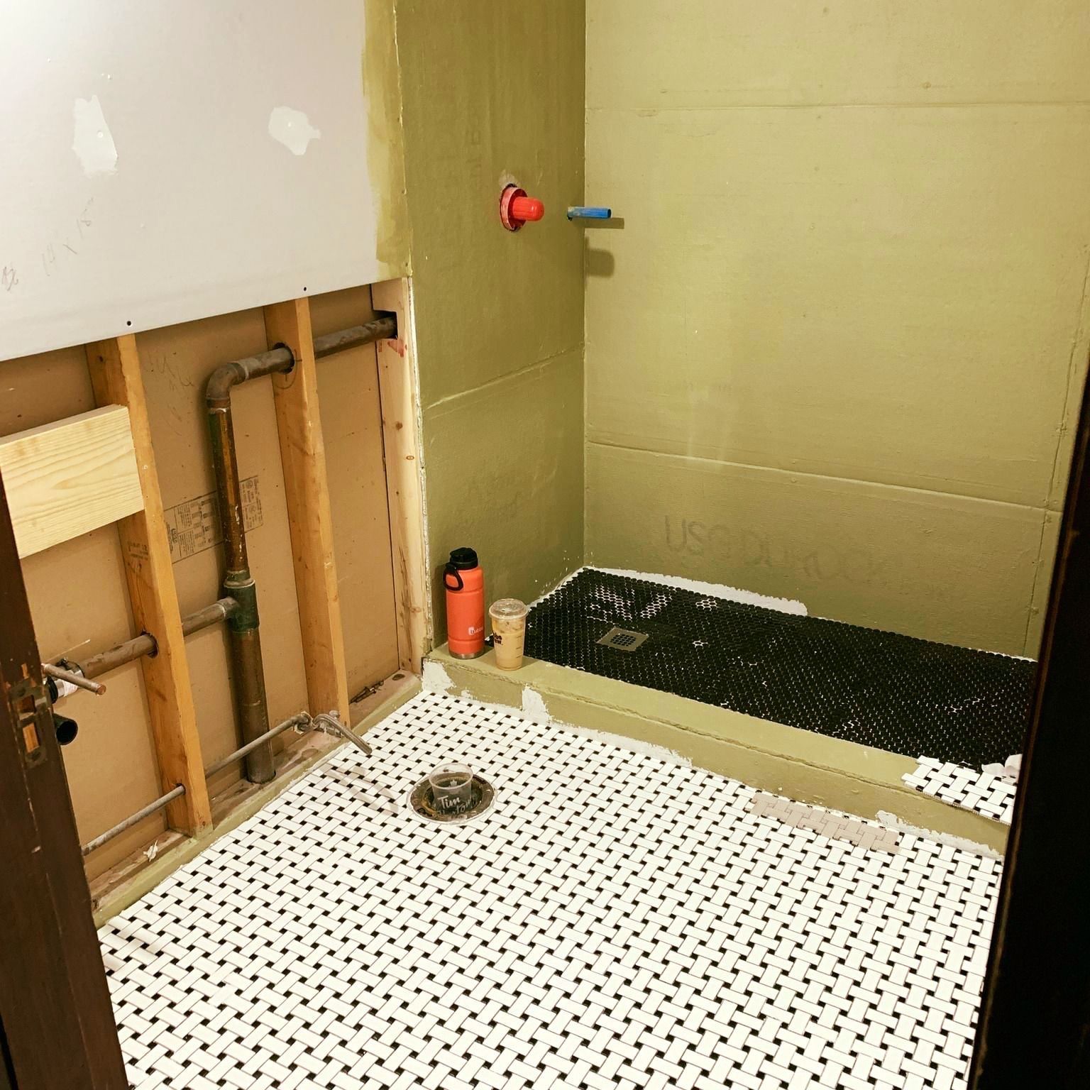 Partially renovated bathroom with exposed plumbing, tiled shower floor, and beige walls
