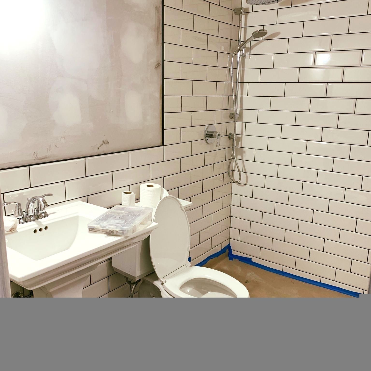 Small bathroom with a sink, toilet, tiled walls, and a shower stall with blue tape along the floor edge