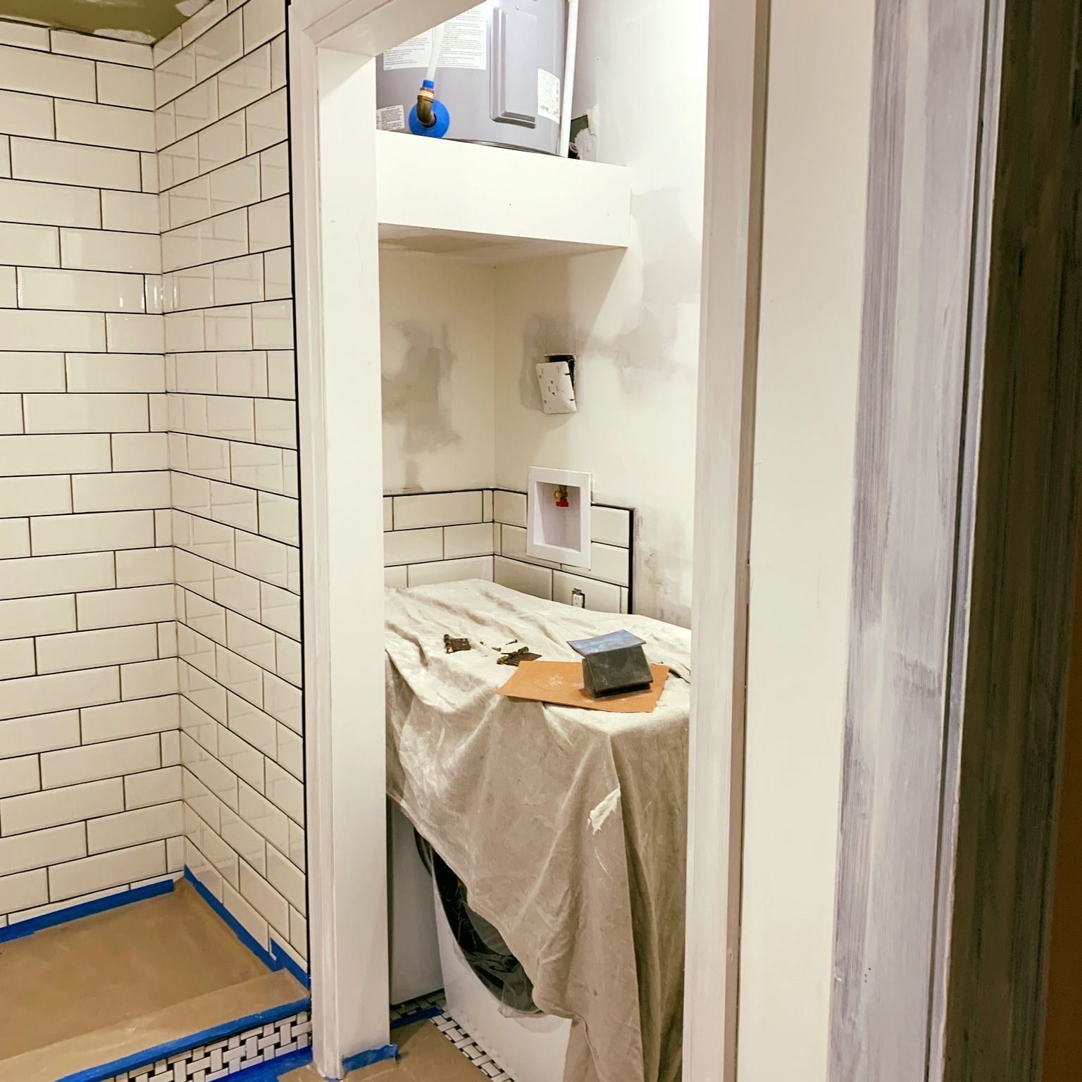 Small bathroom under renovation with white tiled walls, a toilet alcove, and a covered sink with tools on top.