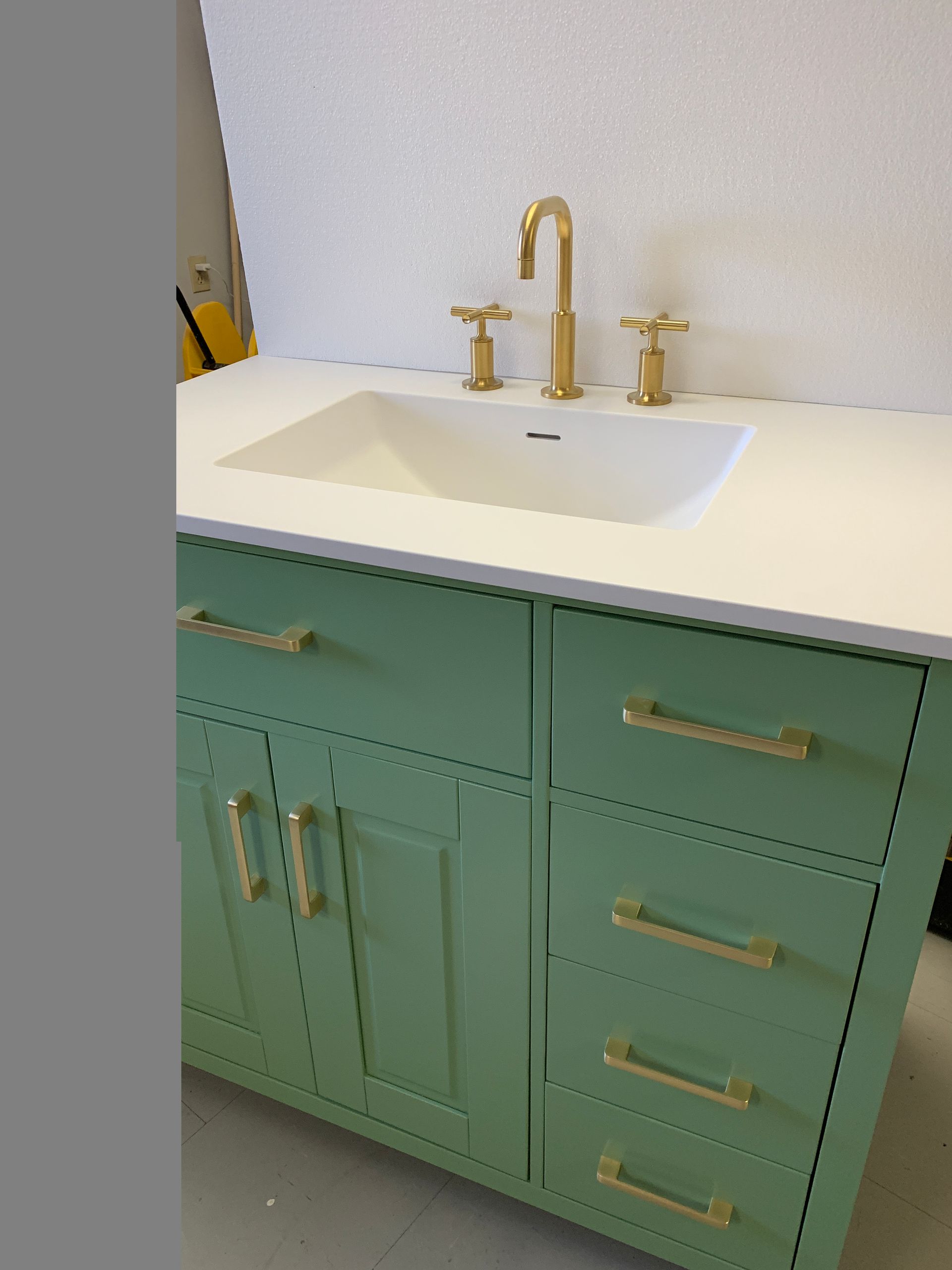 Mint green bathroom vanity with white countertop and gold faucet and handles