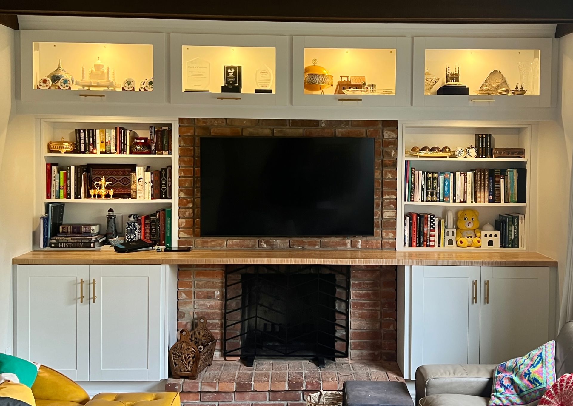 Built-in living room wall with TV, bookshelves, brick fireplace, and lit display niches