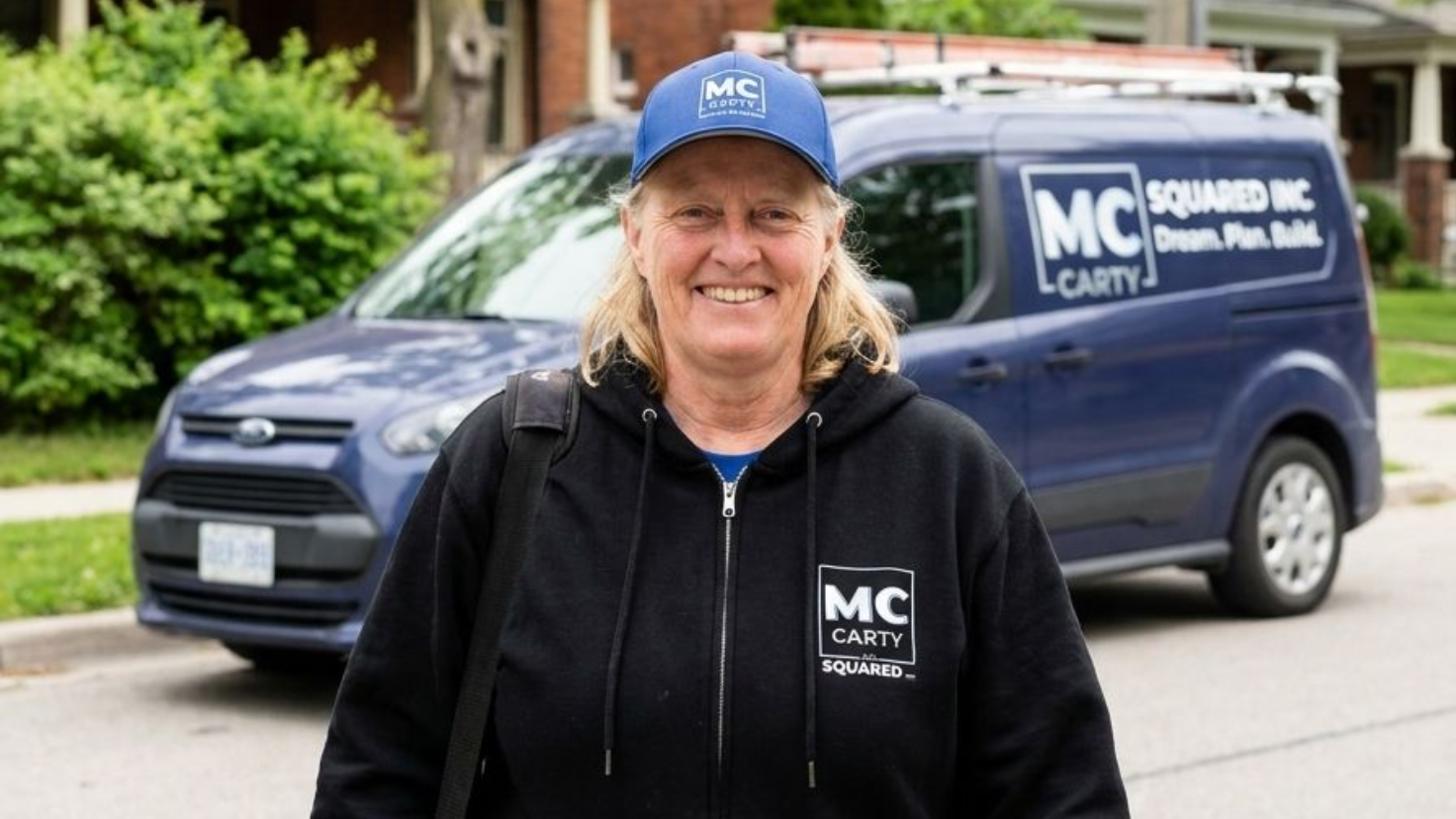 Smiling person in MC Security hoodie and cap standing in front of a branded company van.