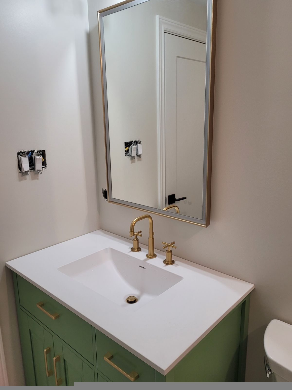 Bathroom vanity with green cabinet, white sink, gold faucet, and mirror on a light wall.