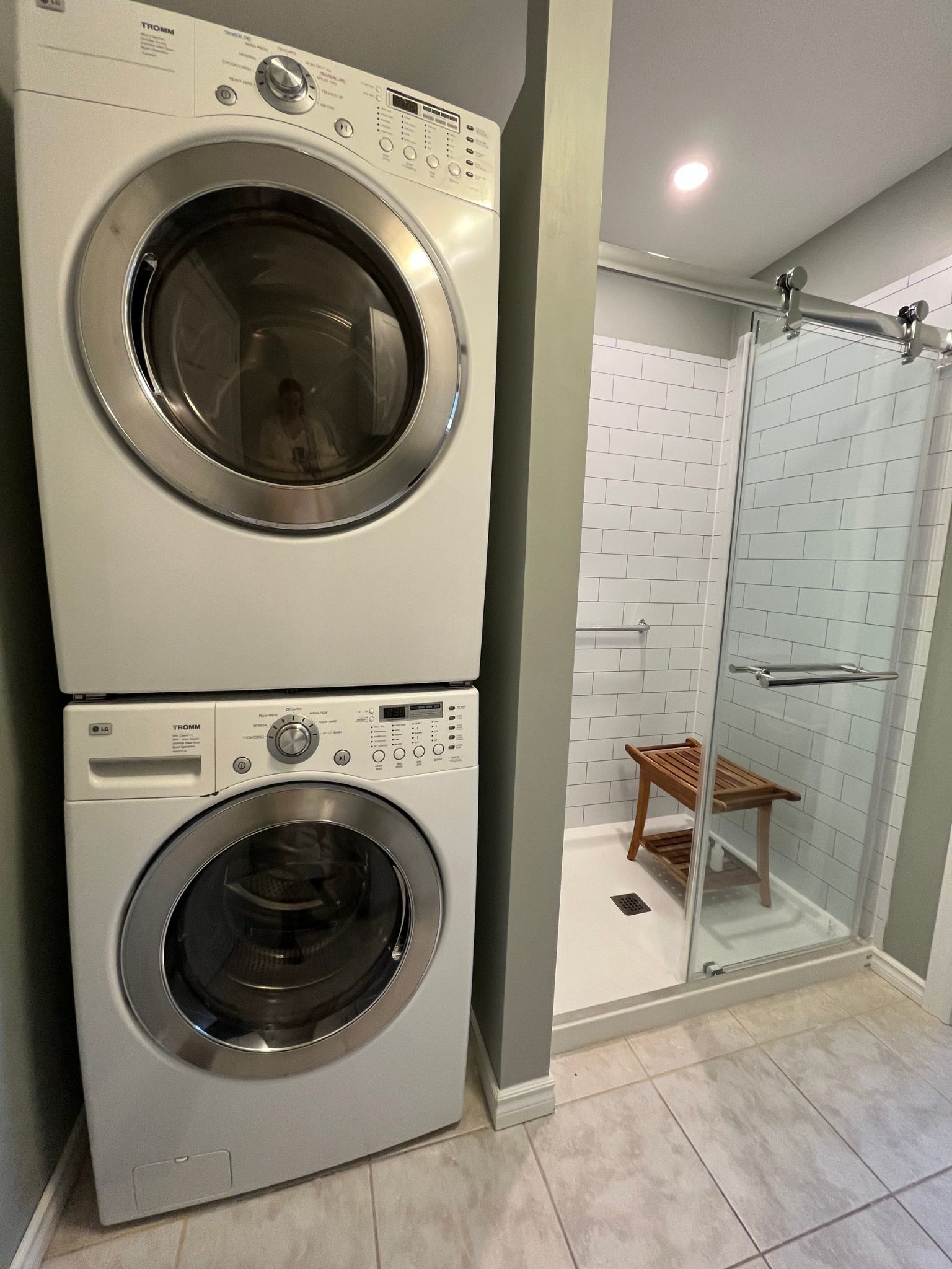 Stacked washer and dryer beside a glass-enclosed shower in a tiled laundry-bathroom space