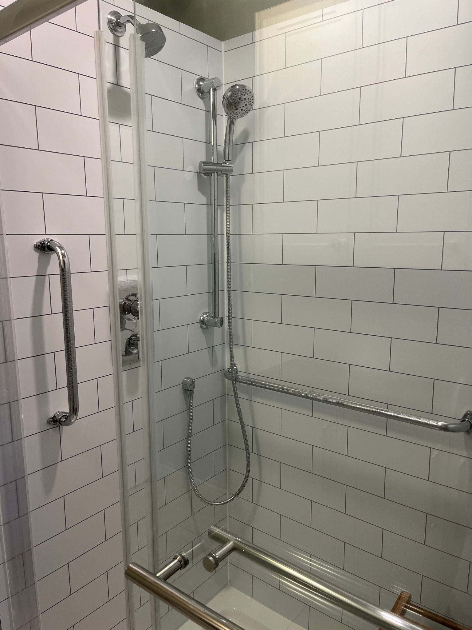 Accessible shower stall with grab bars, shower seat, handheld showerhead, and tiled walls