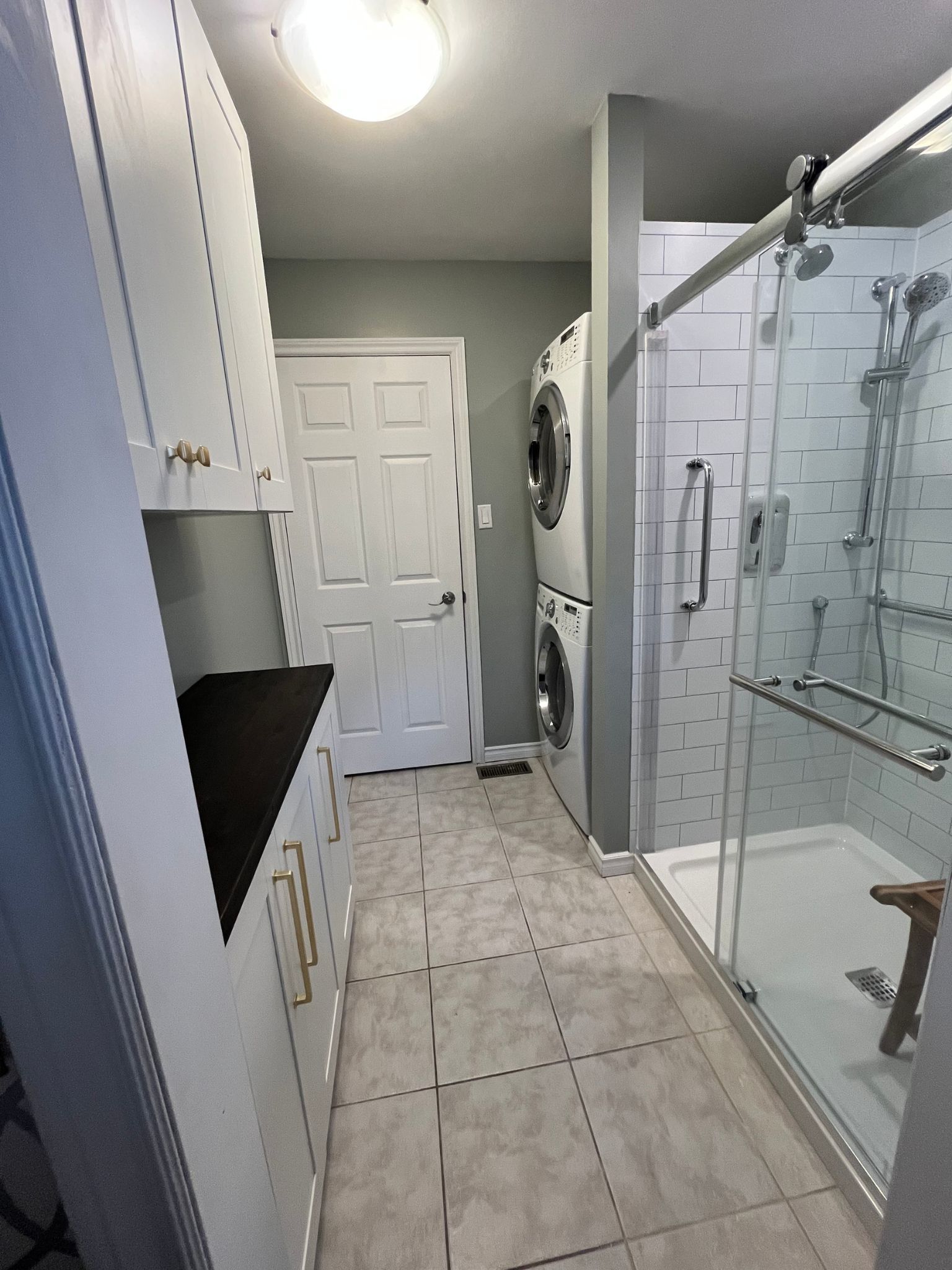 Narrow bathroom with white cabinets, tiled floor, and a glass shower enclosure.