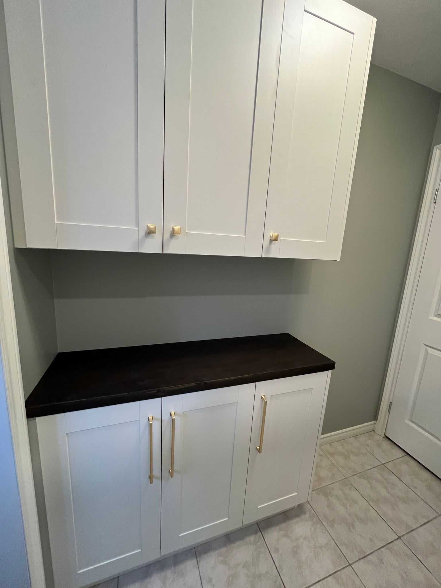 White cabinets with gold pulls and a dark countertop in a tiled laundry room.