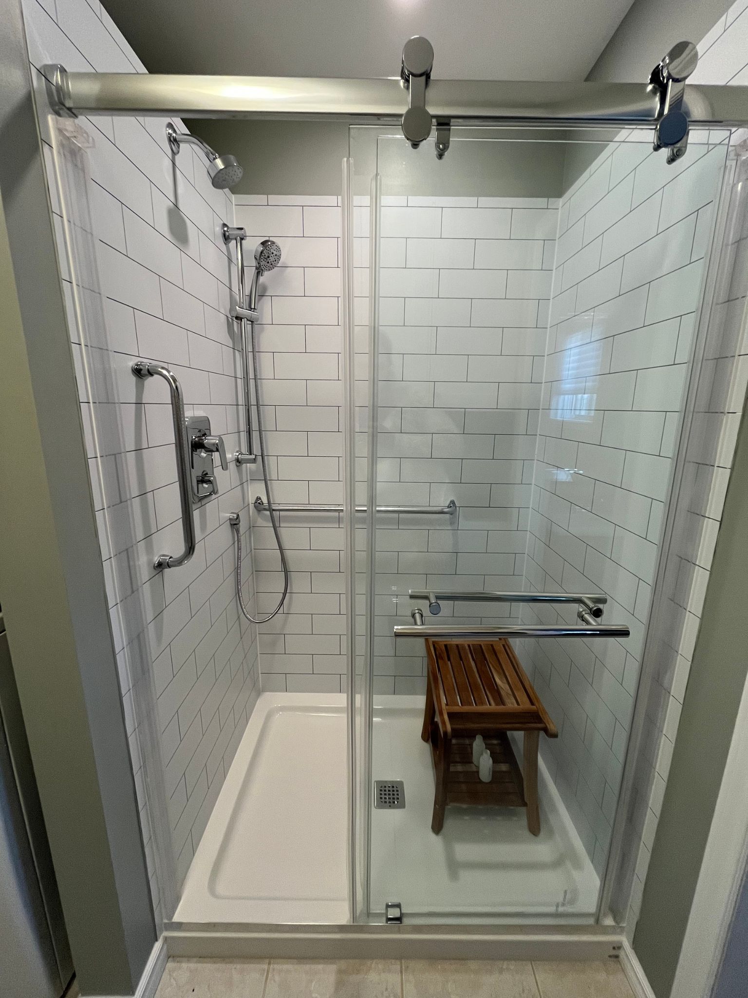 Accessible shower bathroom with glass enclosure, fold-down bench, grab bars, and handheld showerhead