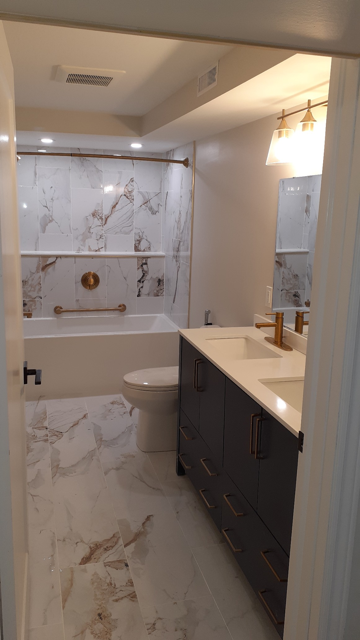 Modern bathroom with white marble tiles, dark vanity, and a tub-shower at the back