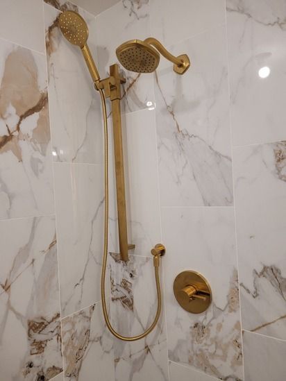 A gold shower head is hanging on a marble wall in a bathroom.
