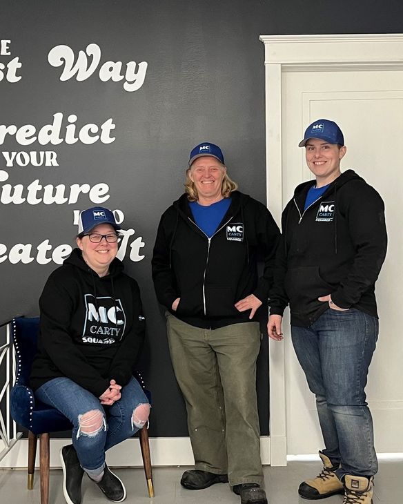 Three people in matching hats and sweatshirts stand in front of a wall with white inspirational text on a black background.